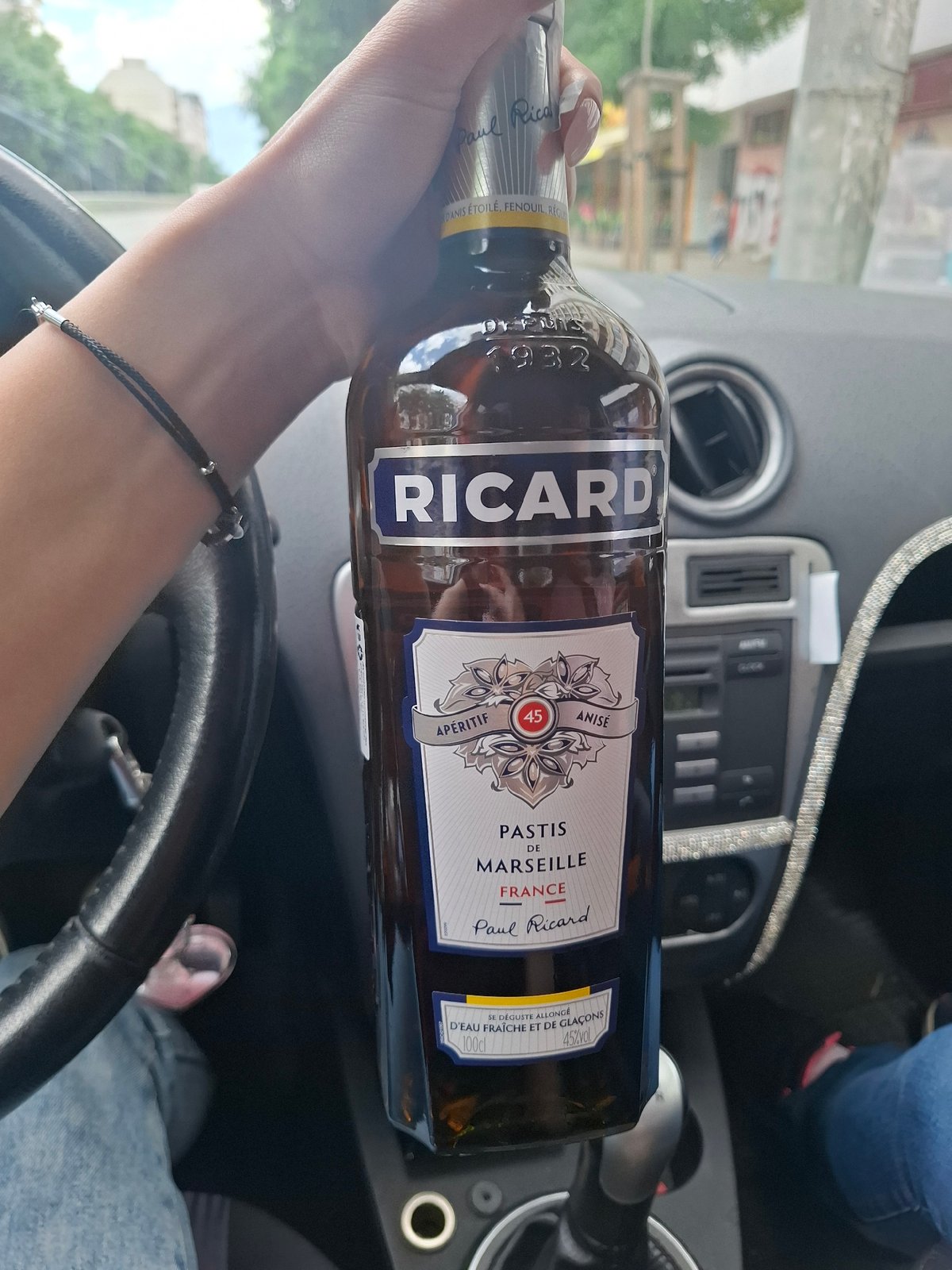 Driver holds French pastis bottle in stationary car
