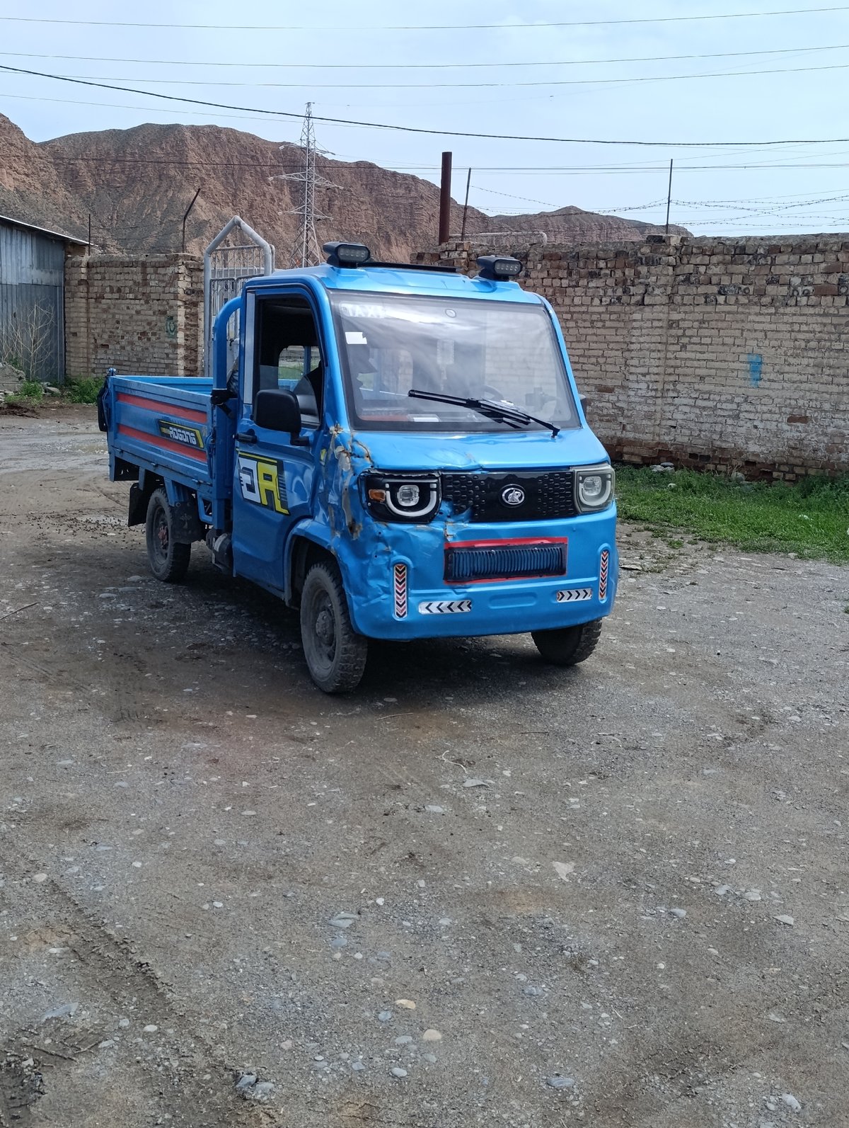 Worn three-wheeled blue truck parked on gravel in Naryn City