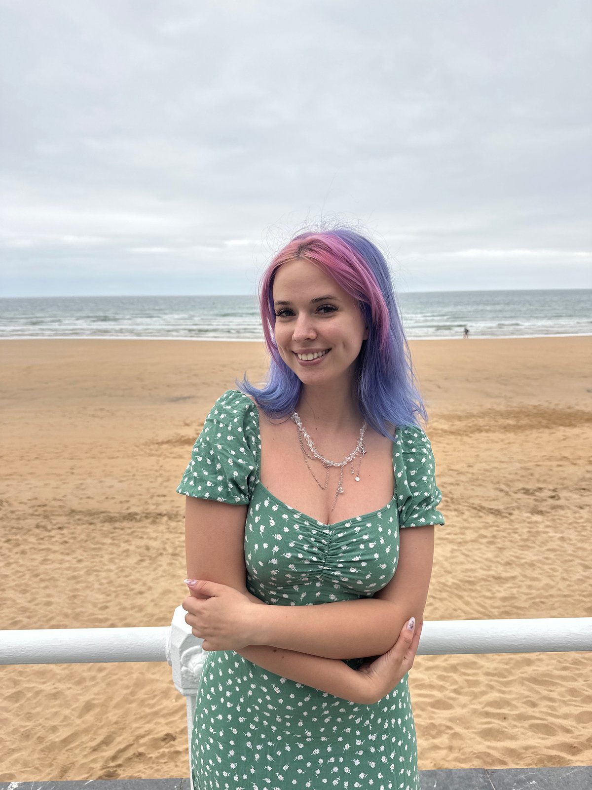Woman poses at Gijón beach promenade under overcast evening sky
