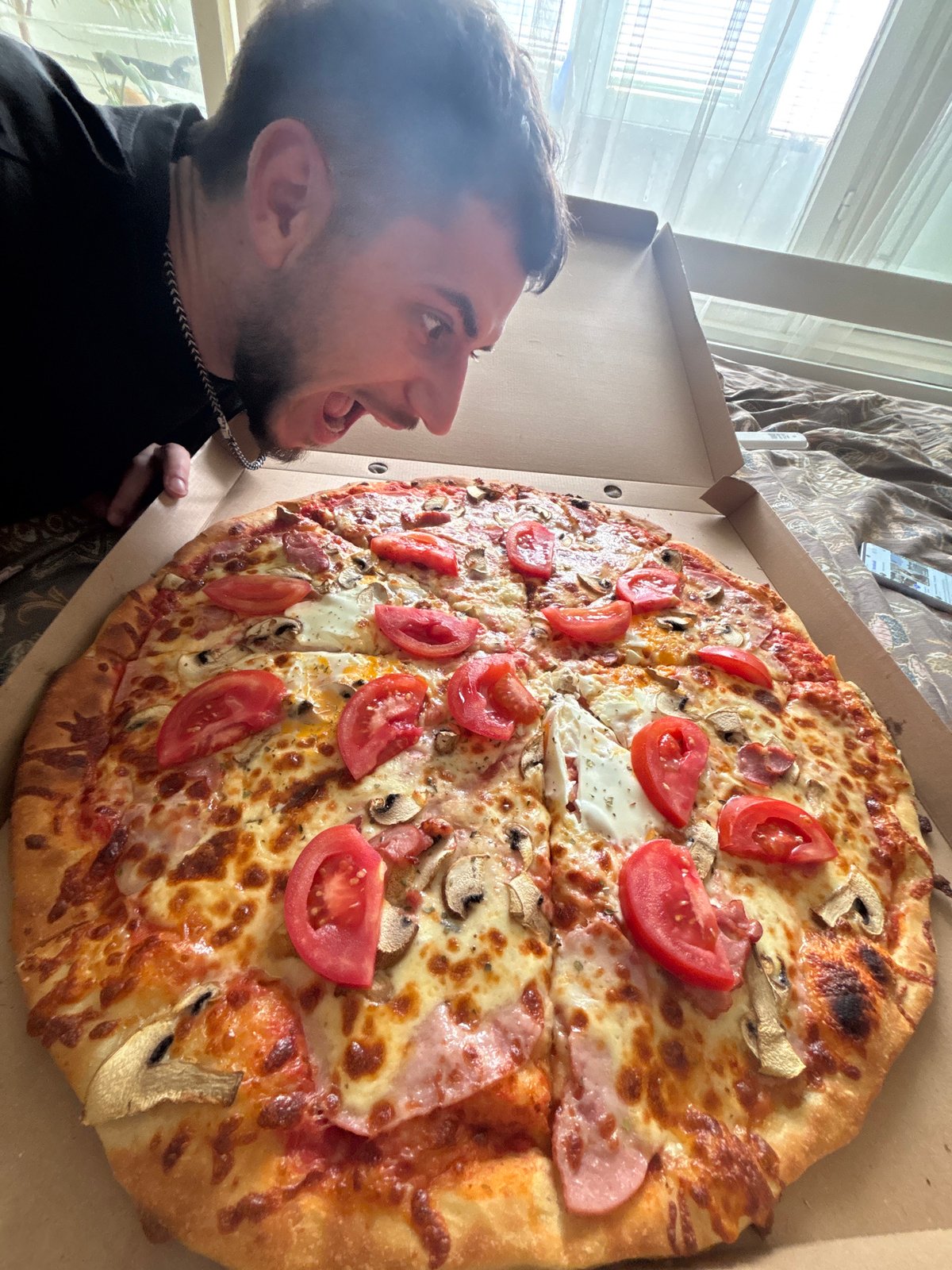 Man examines large topped pizza outdoors in black shirt