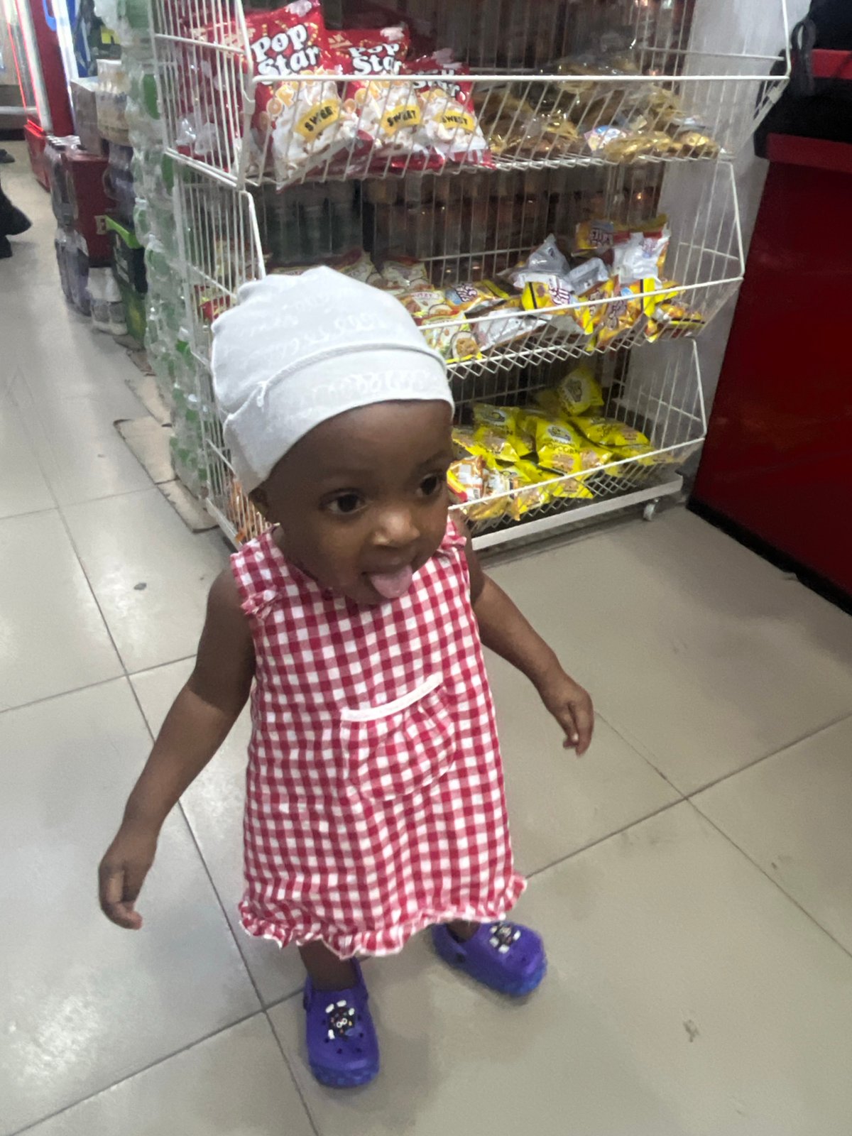 Toddler in checkered dress spotted playing in Nigerian grocery stores