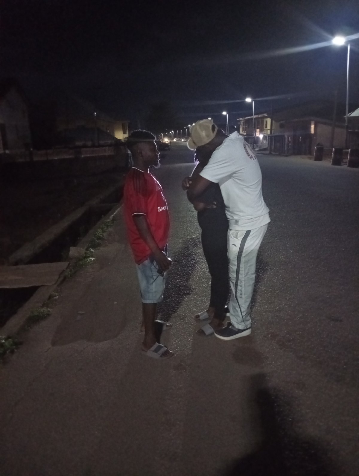 Two people interact on nighttime street in Jos, Nigeria