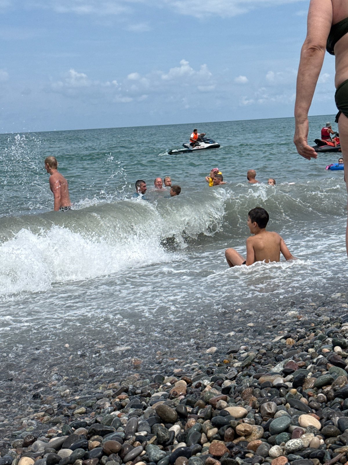 Sailboat, jet ski, and beach crowd on a busy coastal day