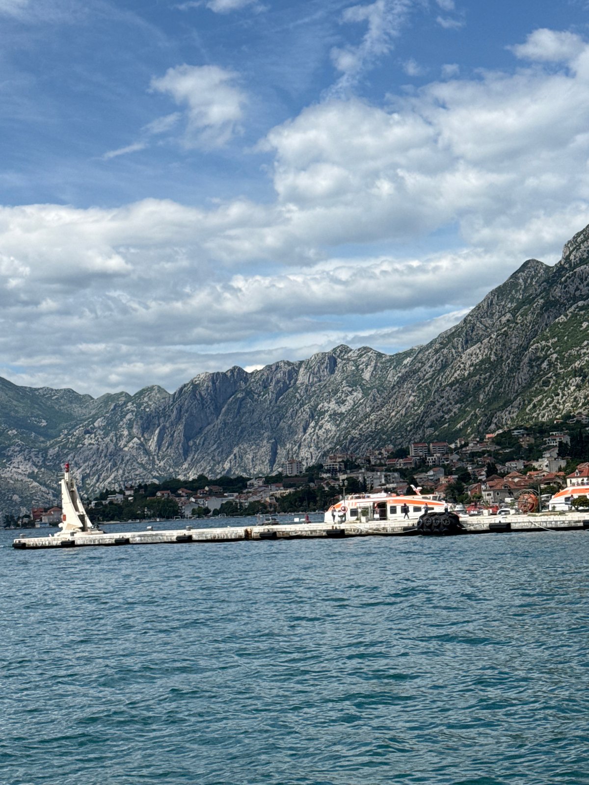 Crowds gather at Kotor harbor pier amid mountain backdrop