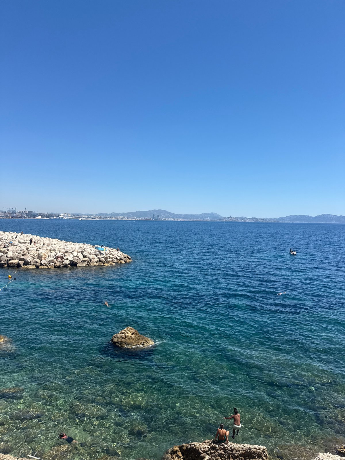 Sunny day along a rocky coastal path near a city.