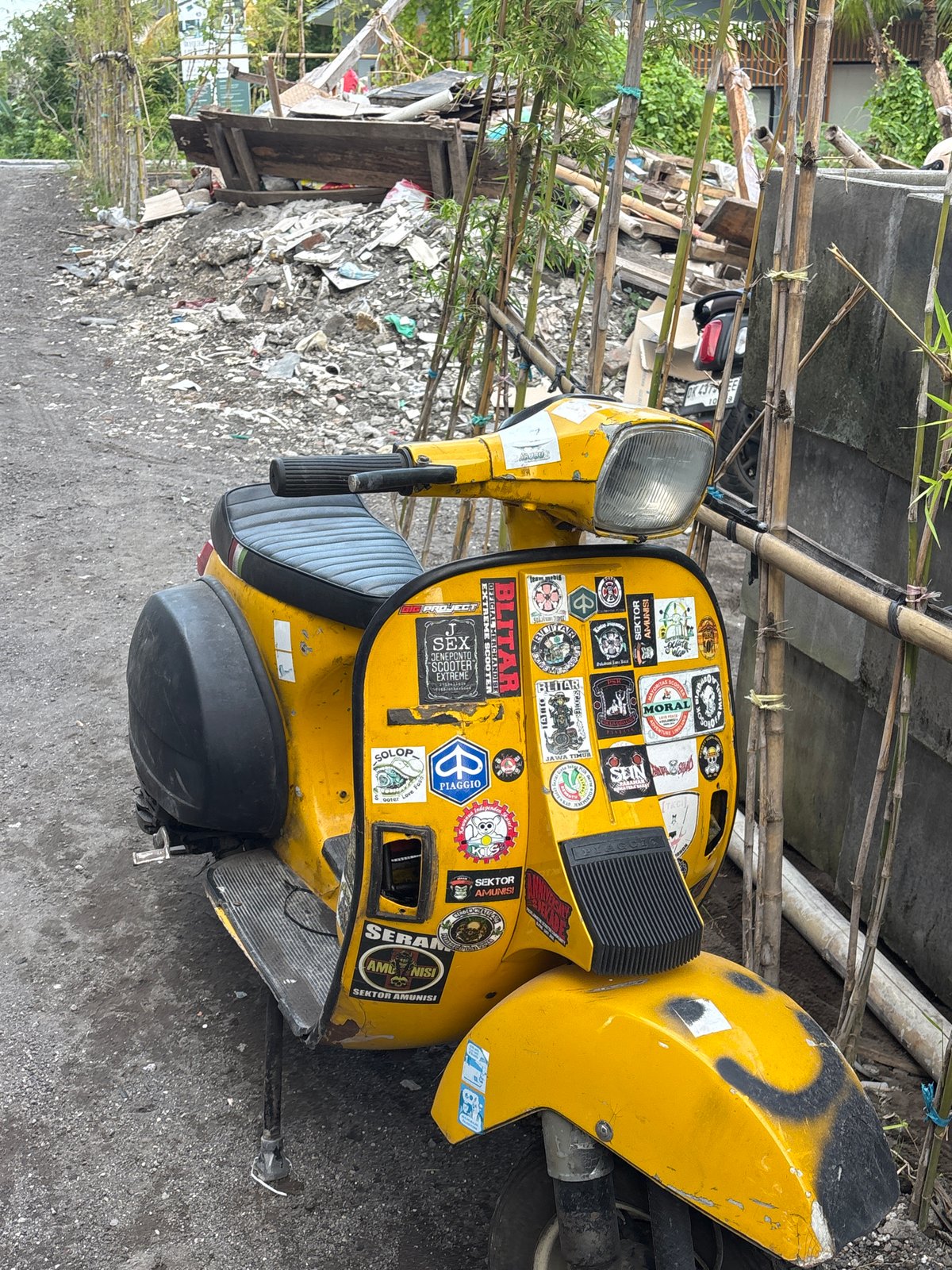 Sticker-covered yellow Vespa spotted amid debris in Mengwi, Indonesia