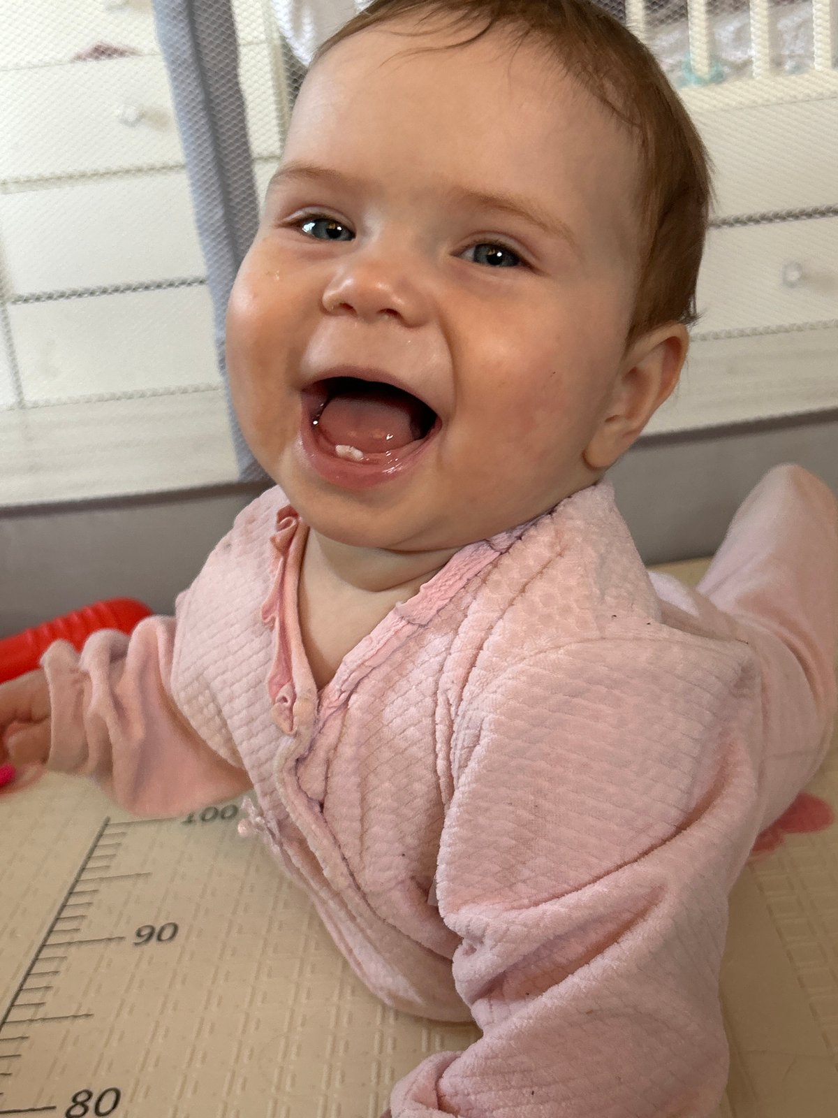 Baby in pink outfit smiles on mat in Rusalevka