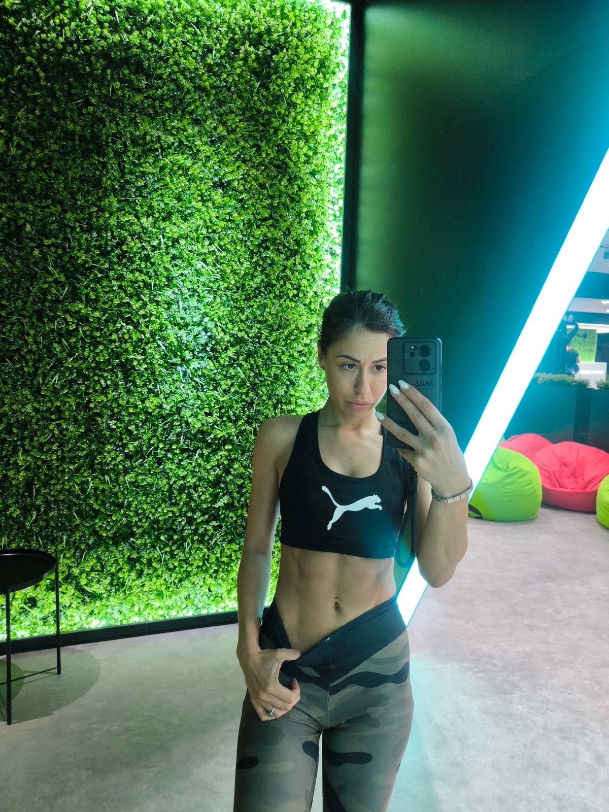 Person takes selfie against decorative wall with green foliage