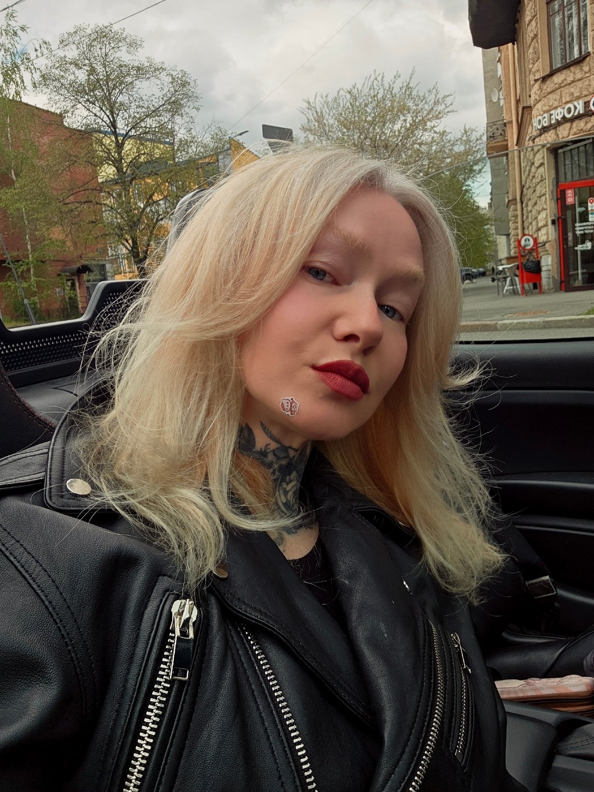 Woman photographed in car, people gather near building in Saint Petersburg