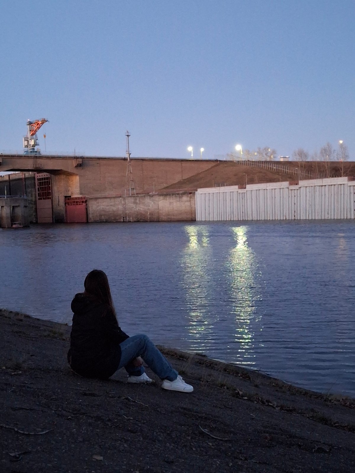 Woman sits by Kama River during sunset in Chaikovsky