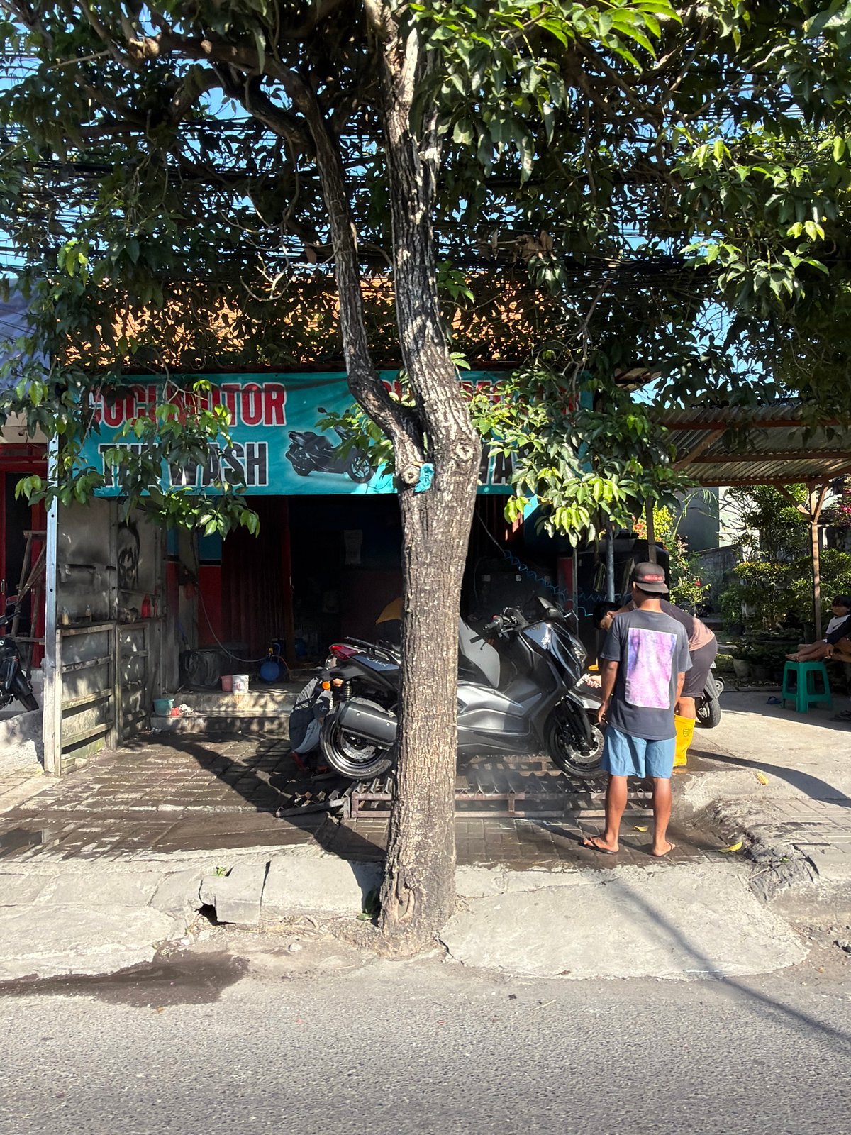 Roadside motorcycle wash spot under a shady tree, North Kuta