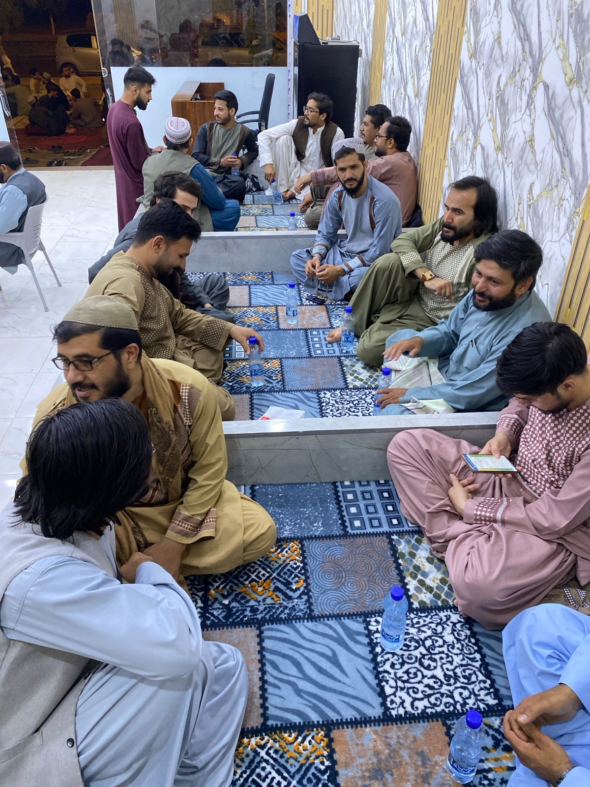 Indoor gathering in Kandahar, traditional dress, floor and table seating
