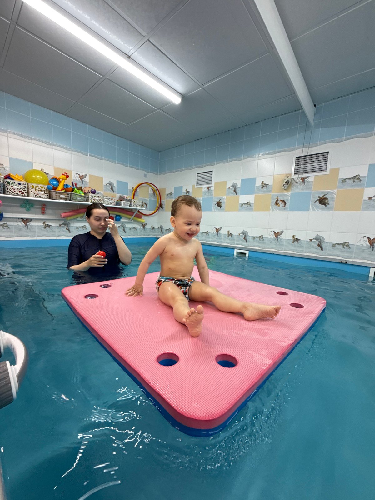 Toddler enjoys swimming activities on pink float in Rusanovo pool