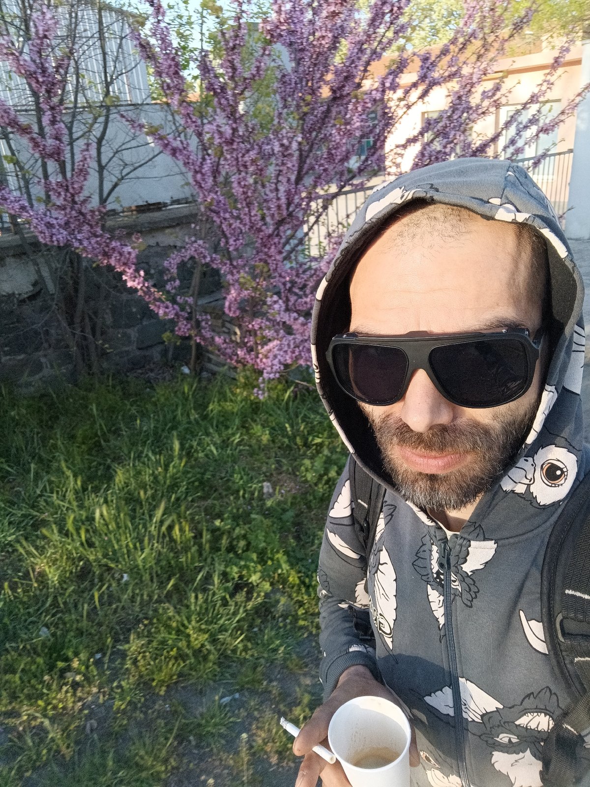 Man takes outdoor selfie with coffee and cigarette