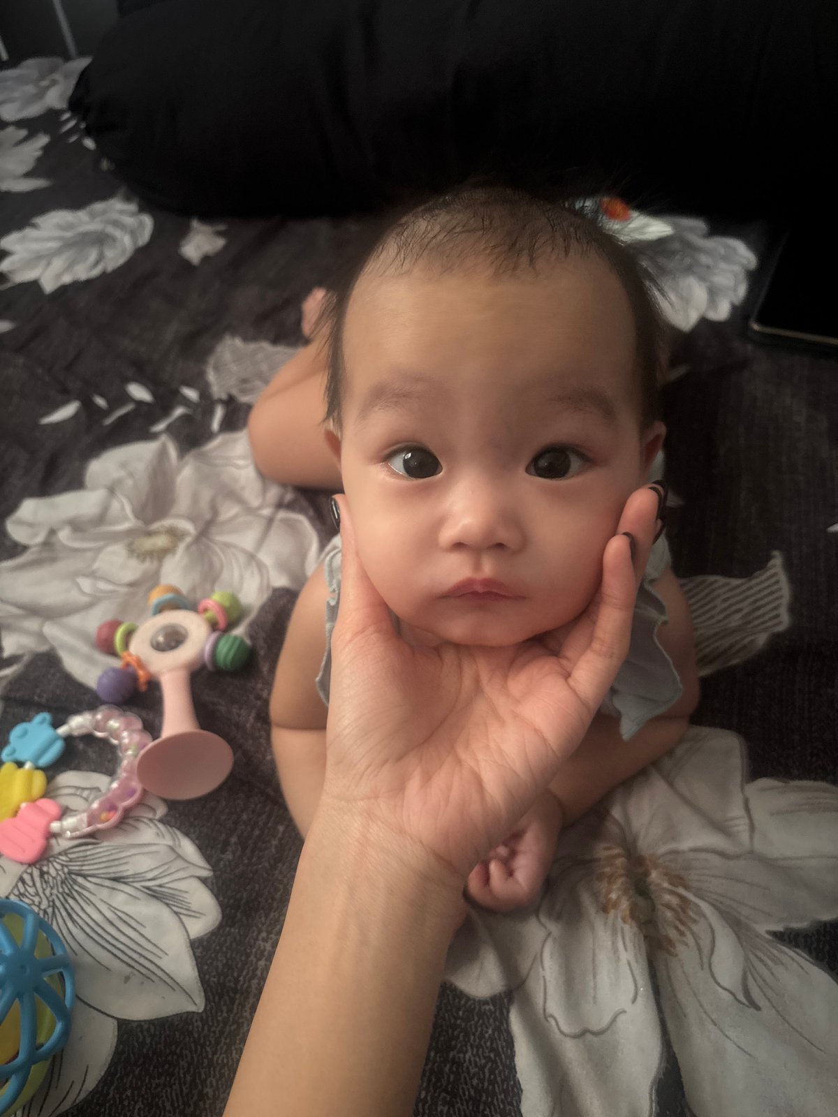 Infant on patterned bed, cheek cradled by a gentle hand