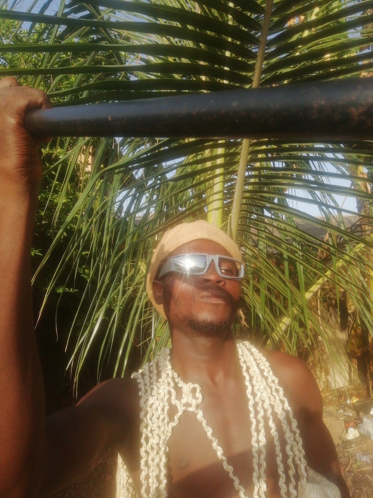 Men in tropical setting, one feeding chickens, another in shell garlands