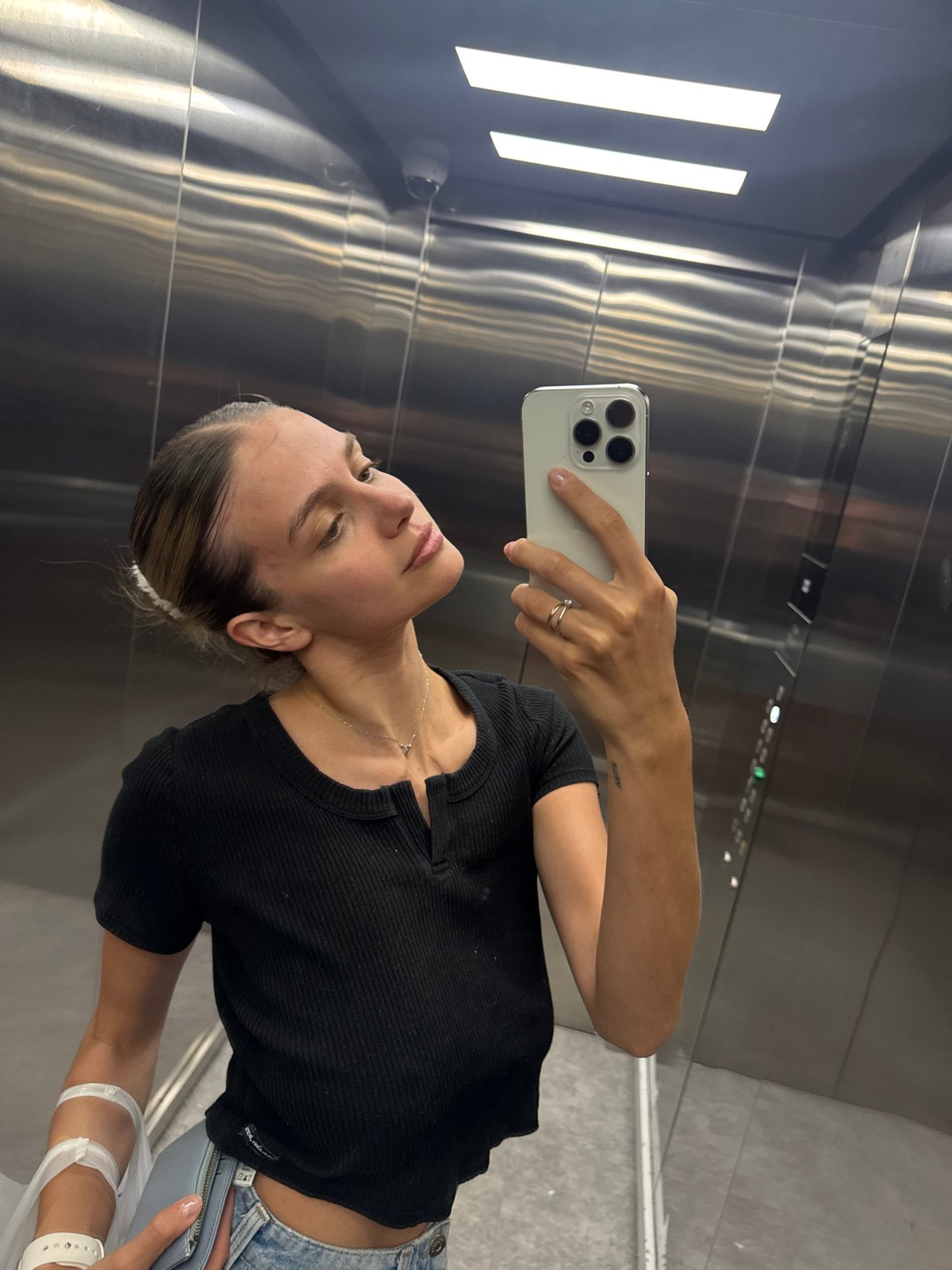 Woman with medical wristband takes elevator selfie, drinks vitamin water