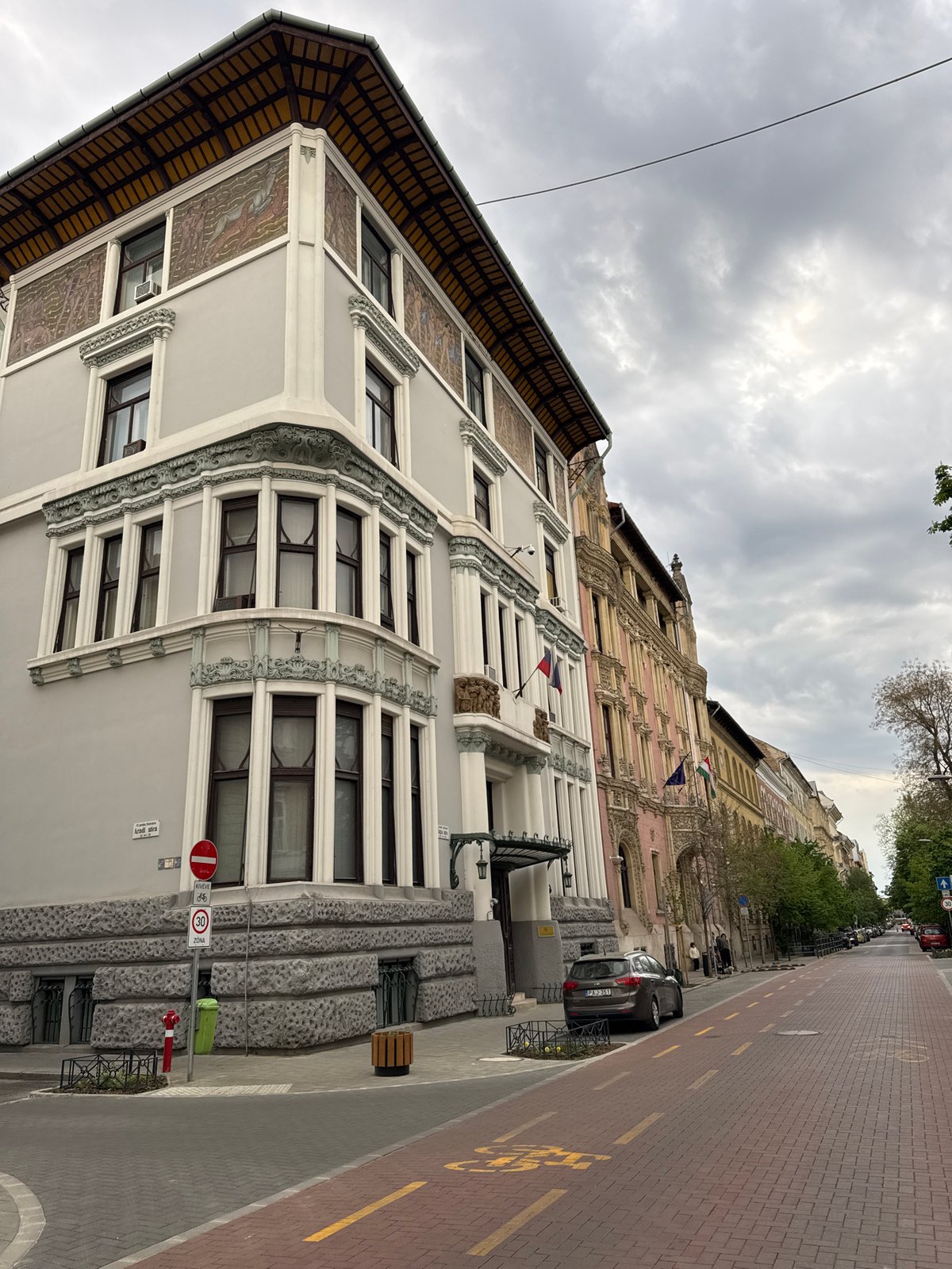 Motorcyclist pauses on ornate Budapest street near white car