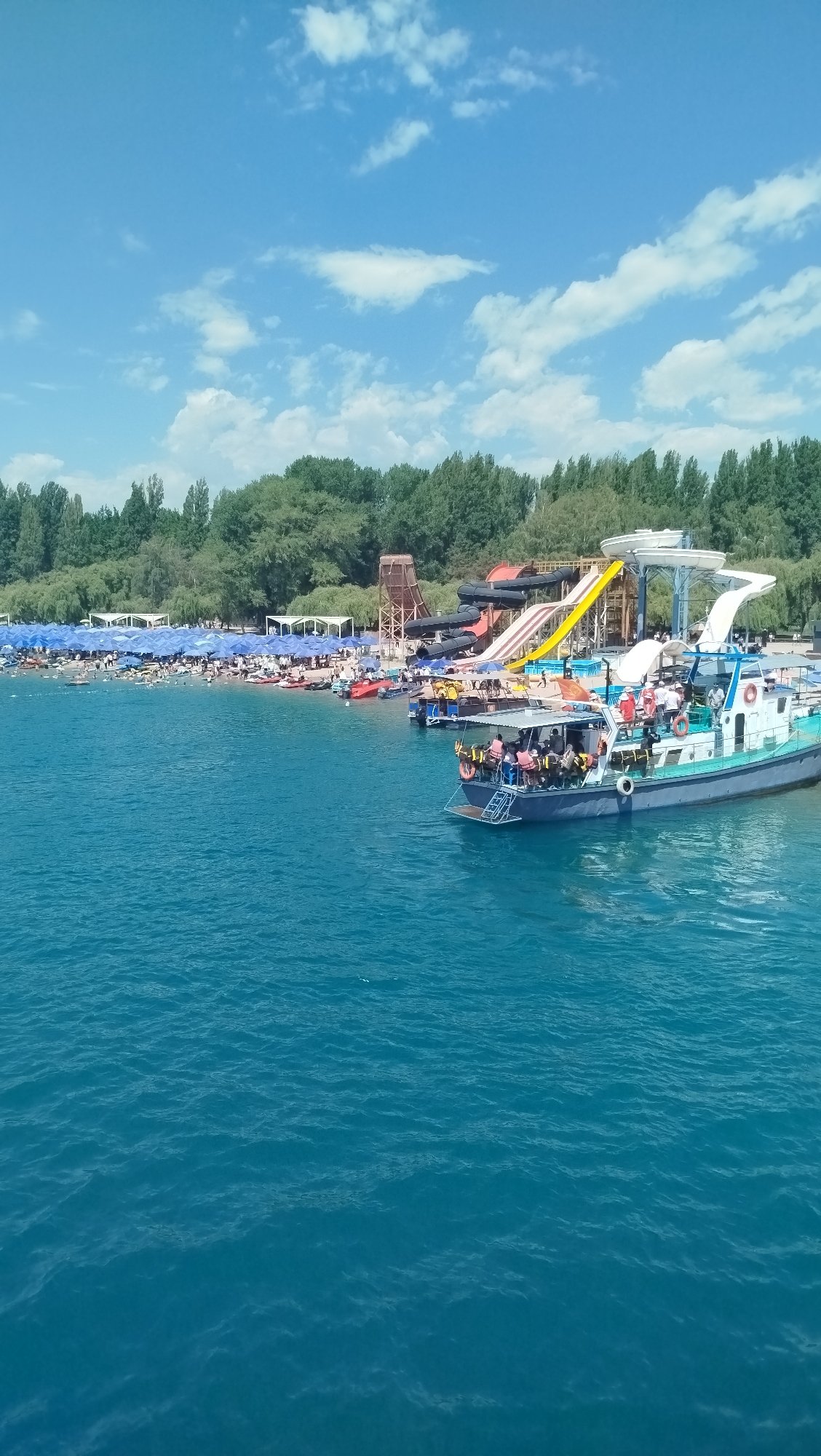 Busy day at a waterfront amusement park with boats and a Ferris wheel