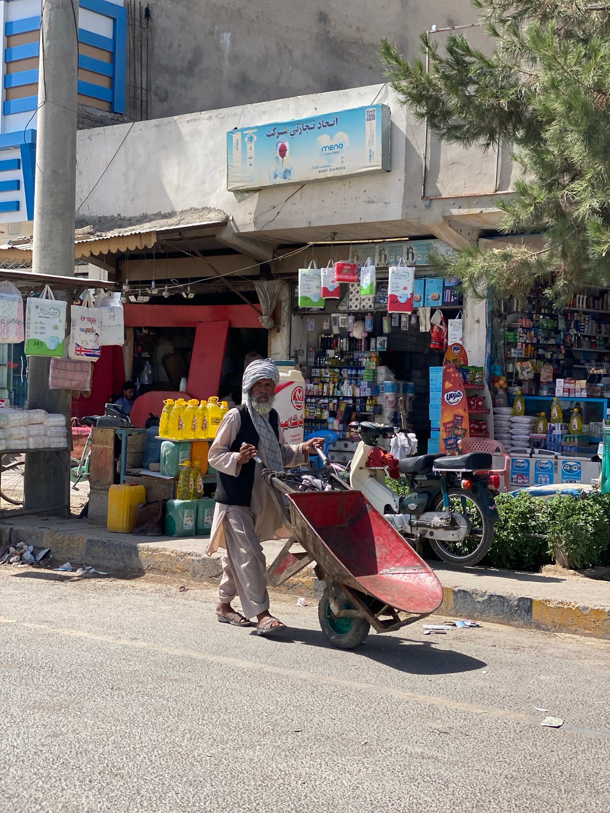 Red wheelbarrow loaded with goods moves through Kandahar streets