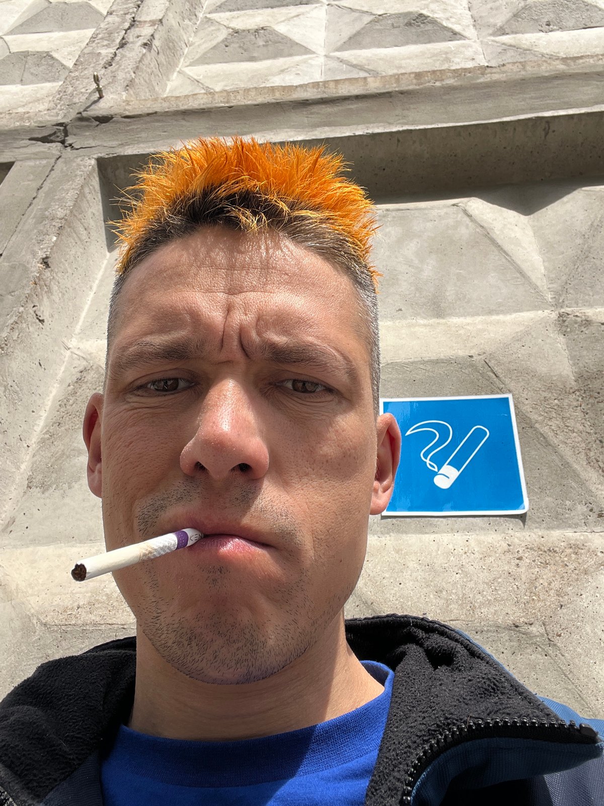 Orange-haired man smoking cigarette near concrete wall in Chaikovsky