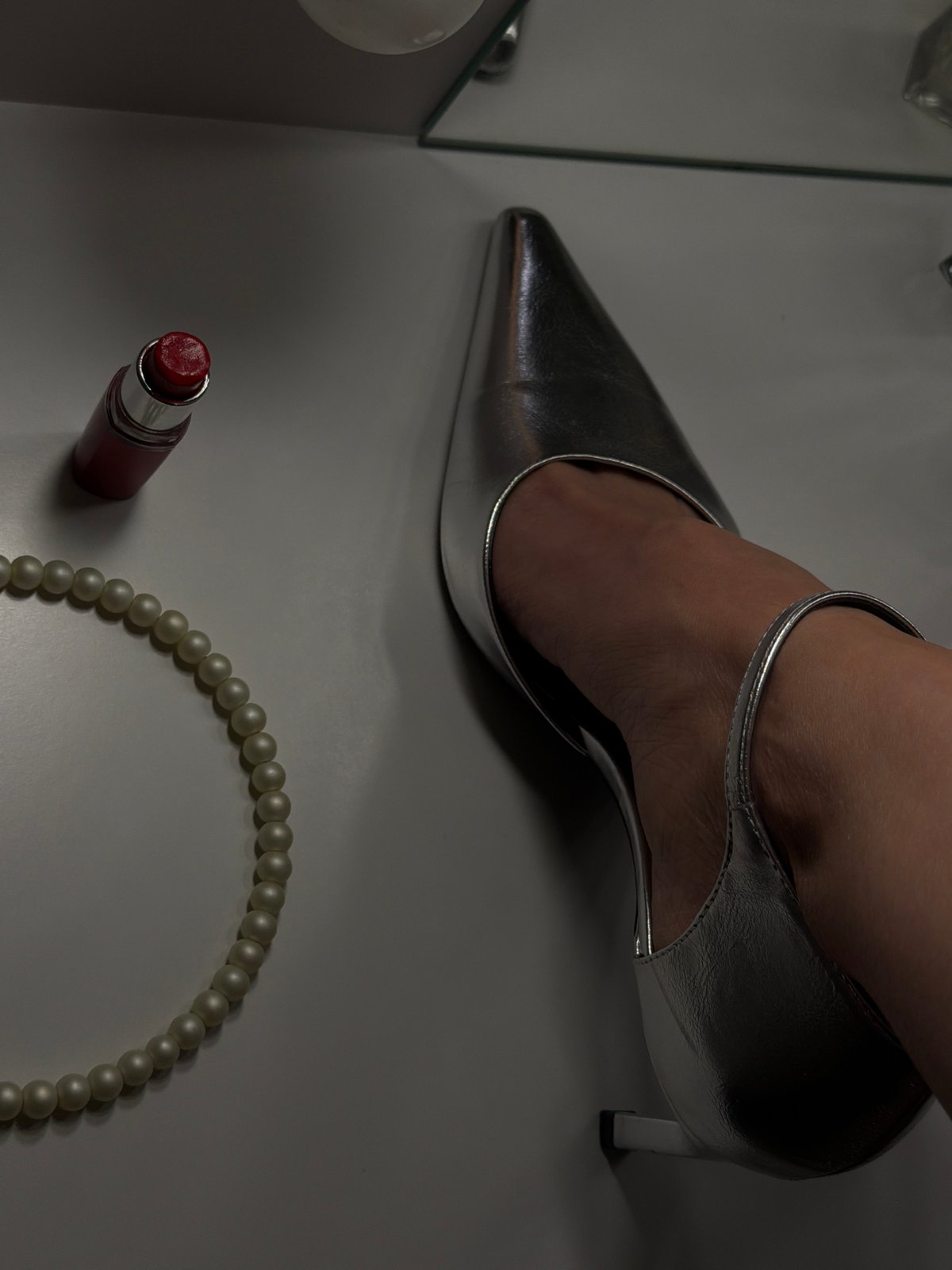 Silver heel, lipstick, pearls arranged on white surface in Bulgaria