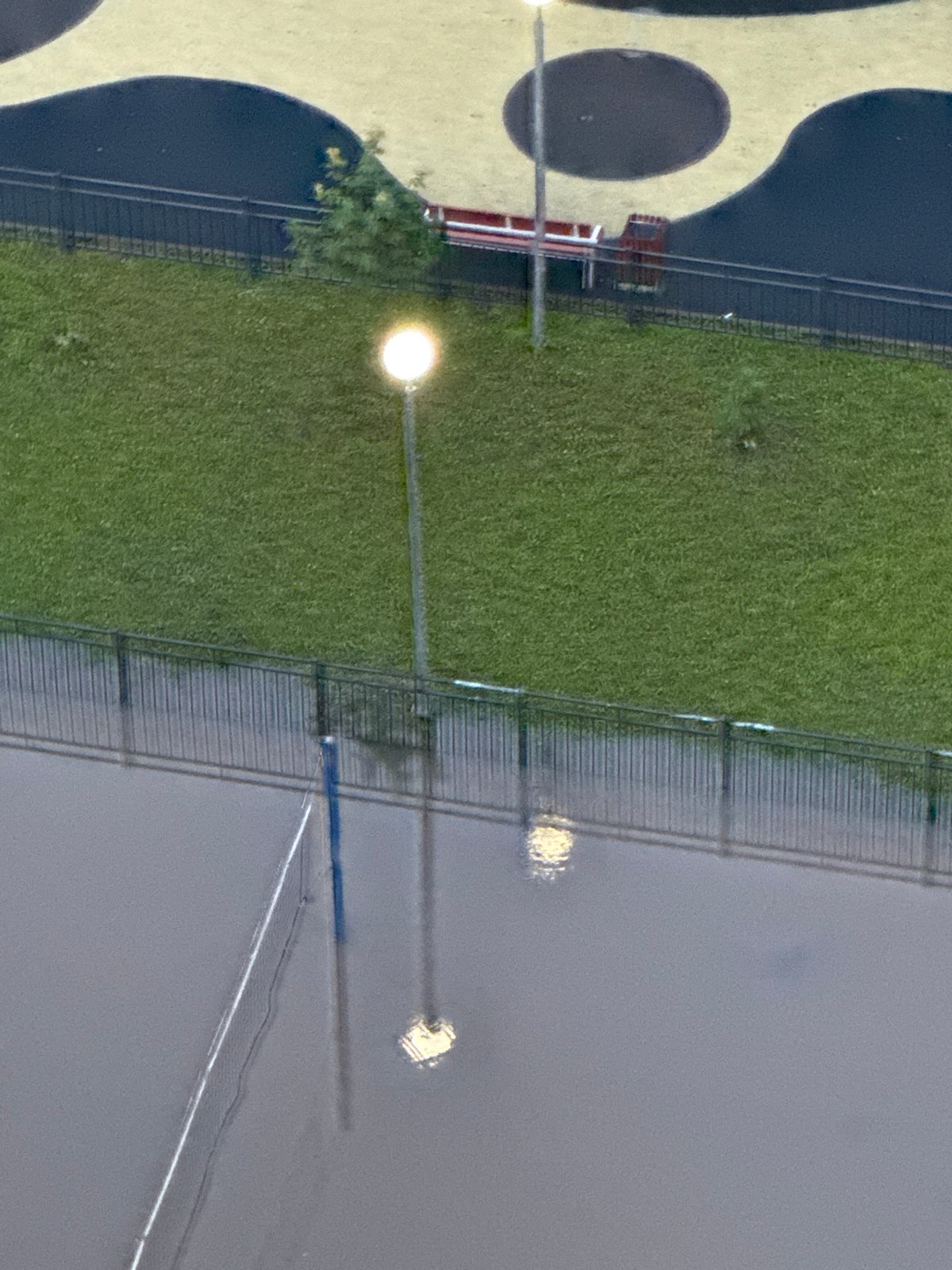 Flooded volleyball court reflects street lamps under stormy Sinyavino skies