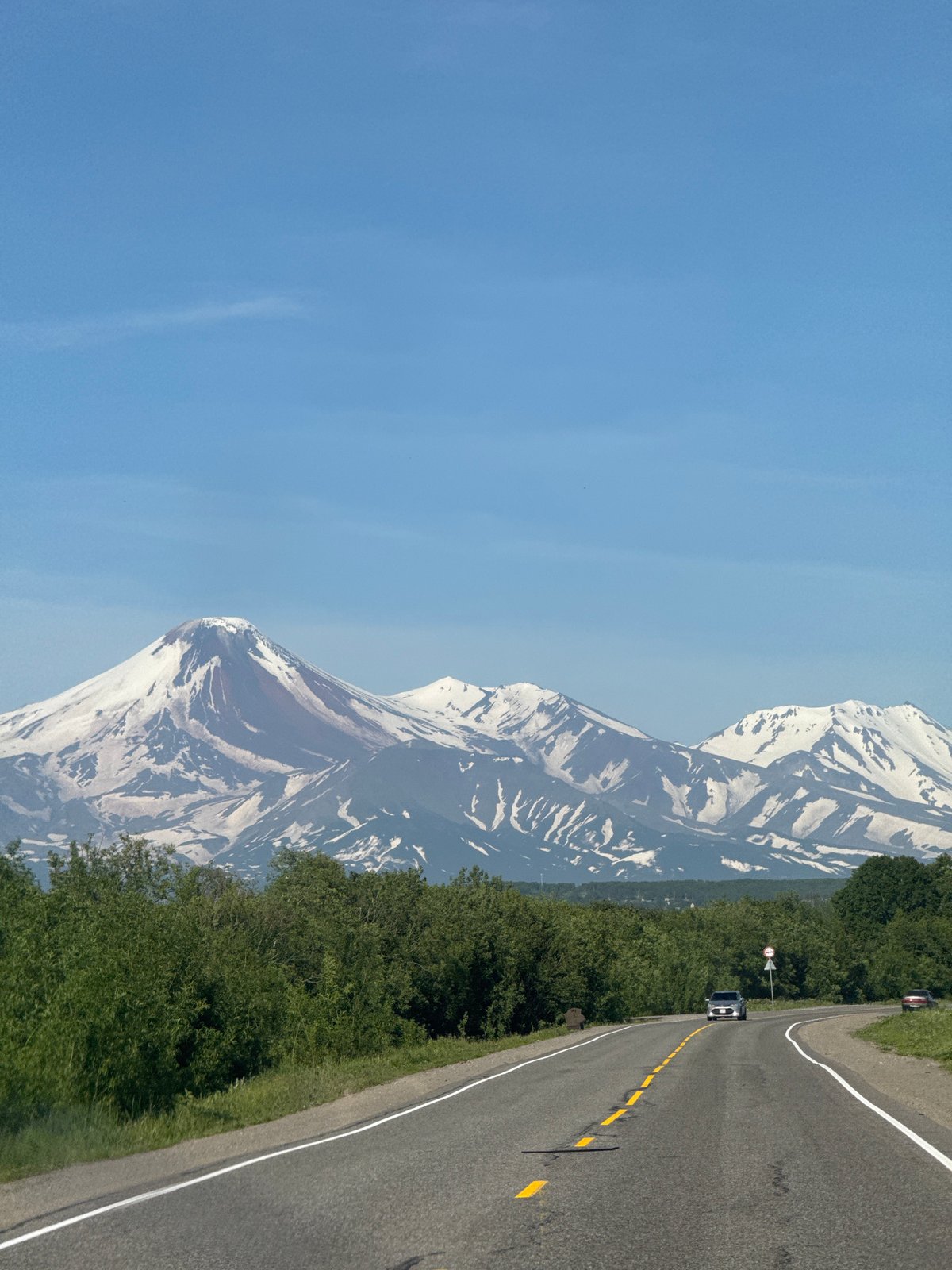 Snow-capped volcanoes loom over a curving road in Kamchatka