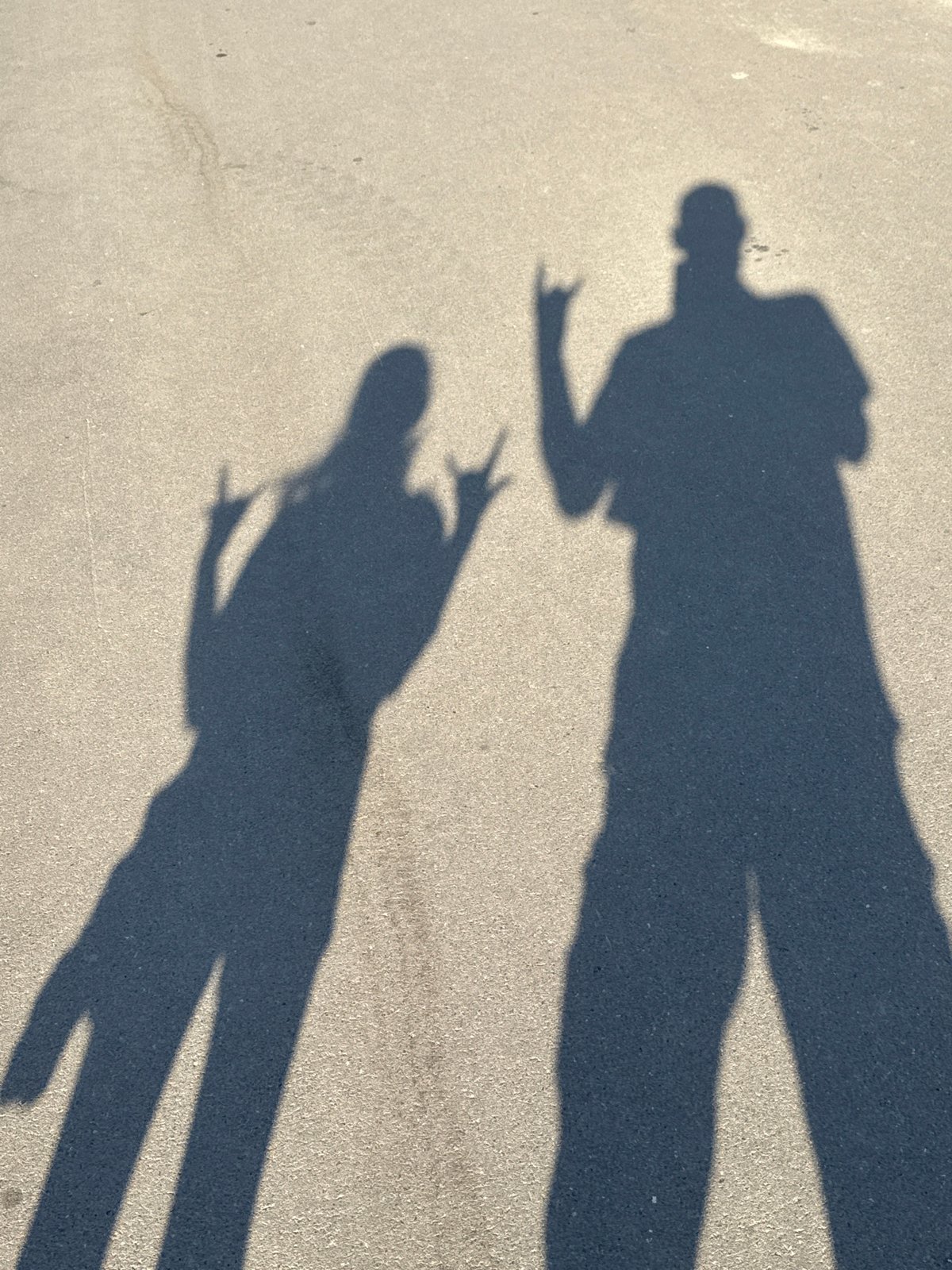 Peace sign shadow and a larger silhouette on asphalt