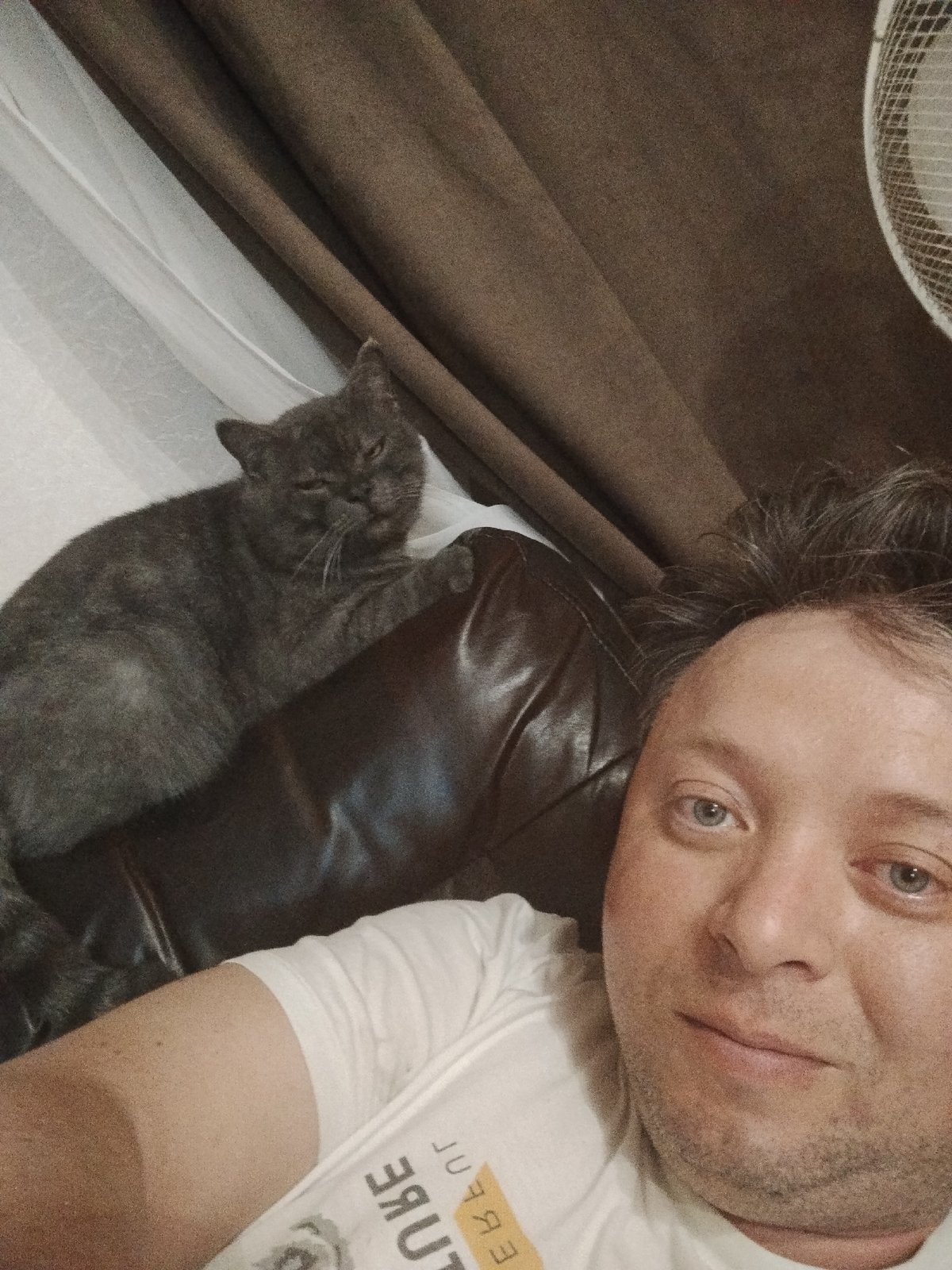 Man takes selfie with gray cat on leather couch