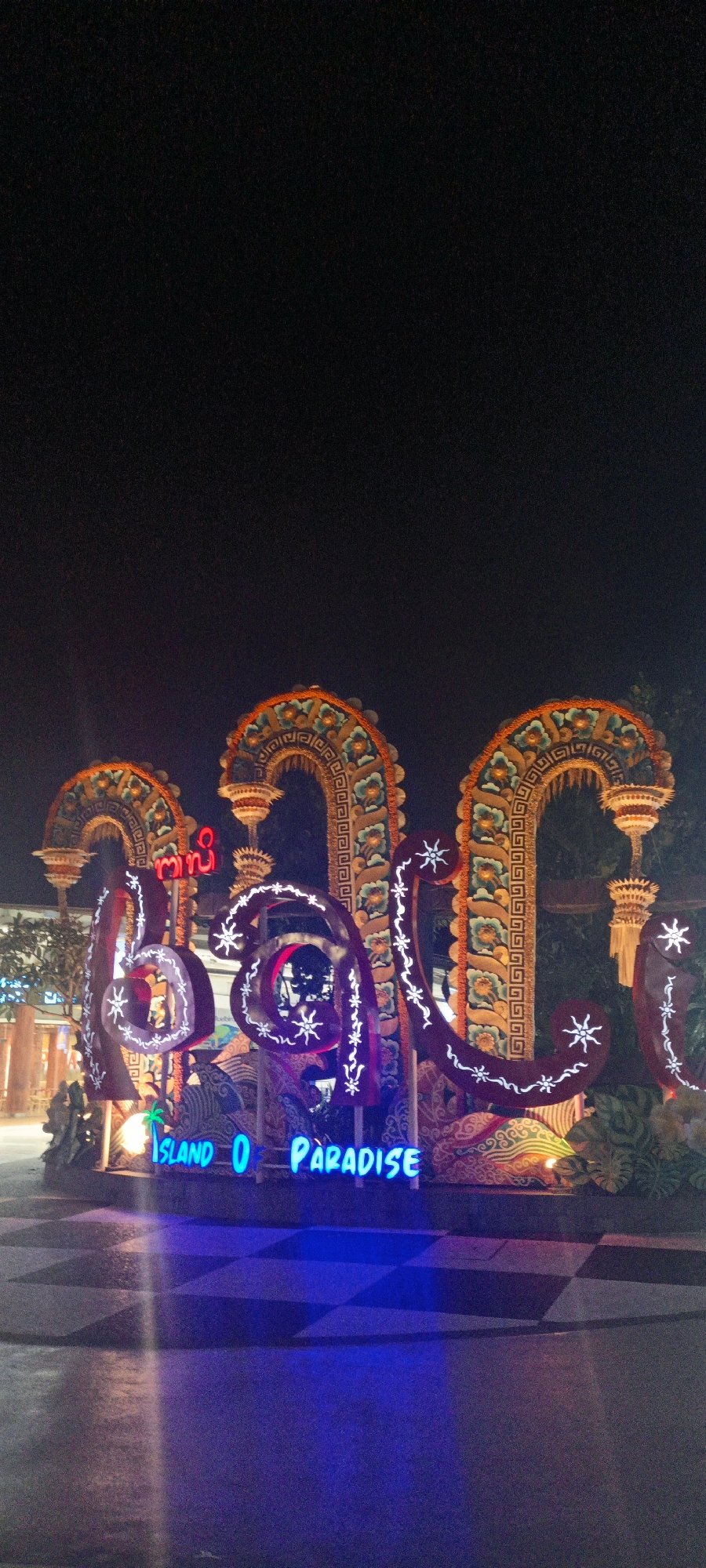 Neon 'Bali Island of Paradise' sign glowing at night in Kuta