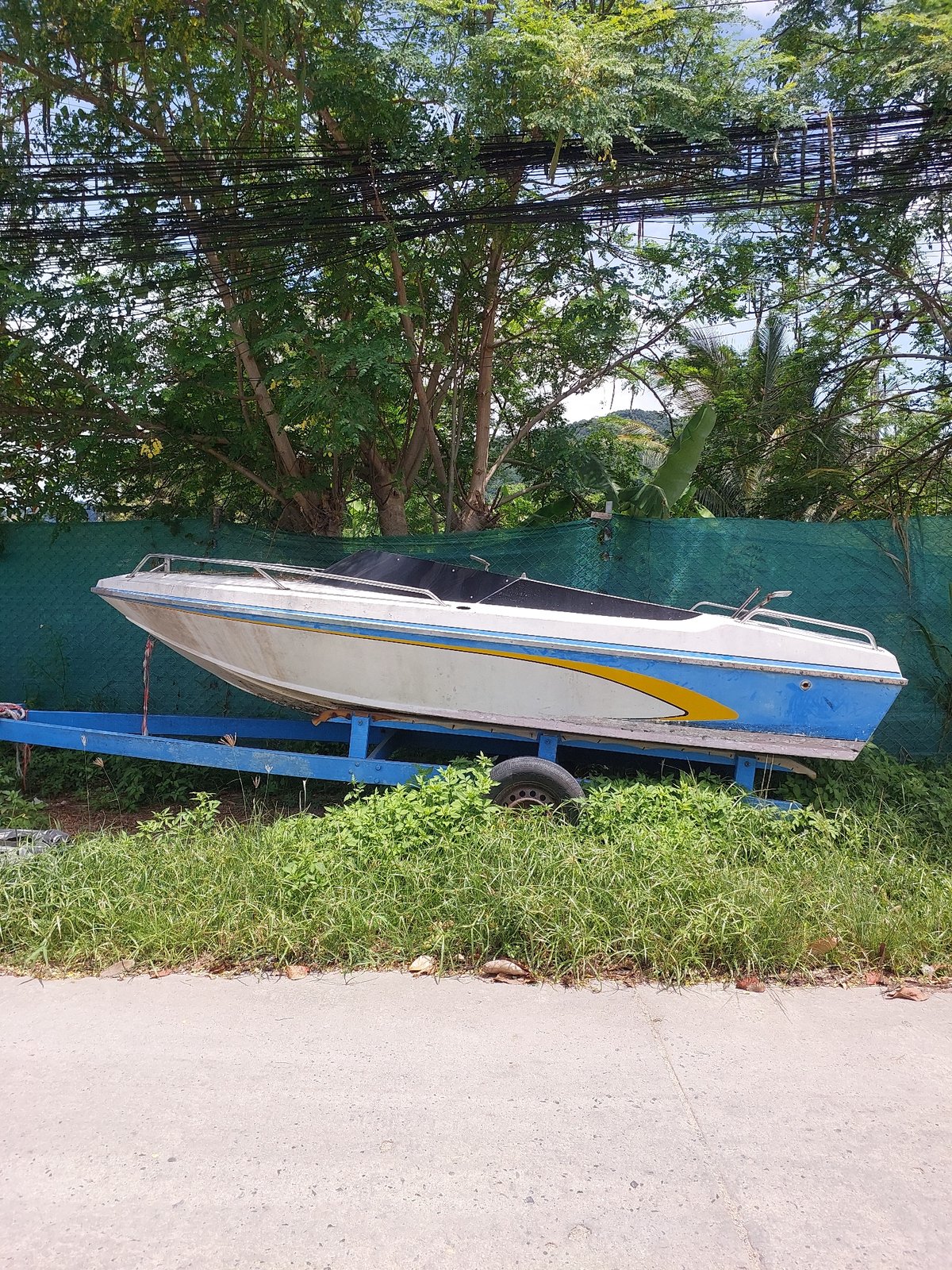 Older motorboat on trailer parked roadside in Baan Tai