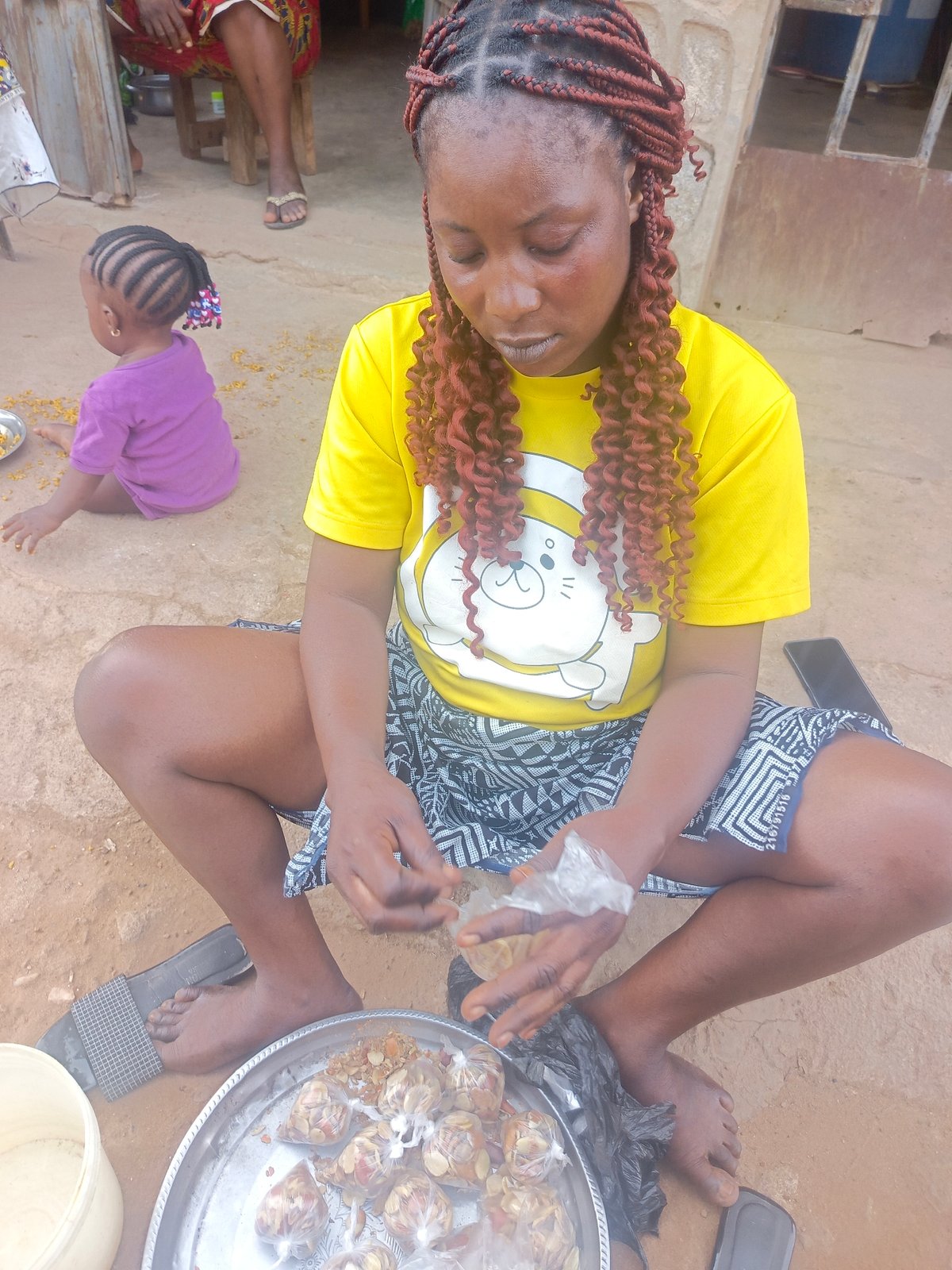 Woman packs food items on ground in Akwanga
