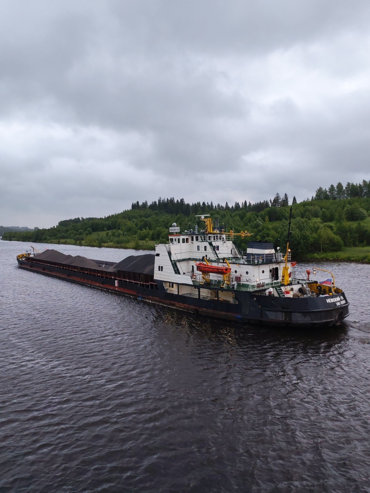 Coal barge navigates a Russian river on an overcast morning