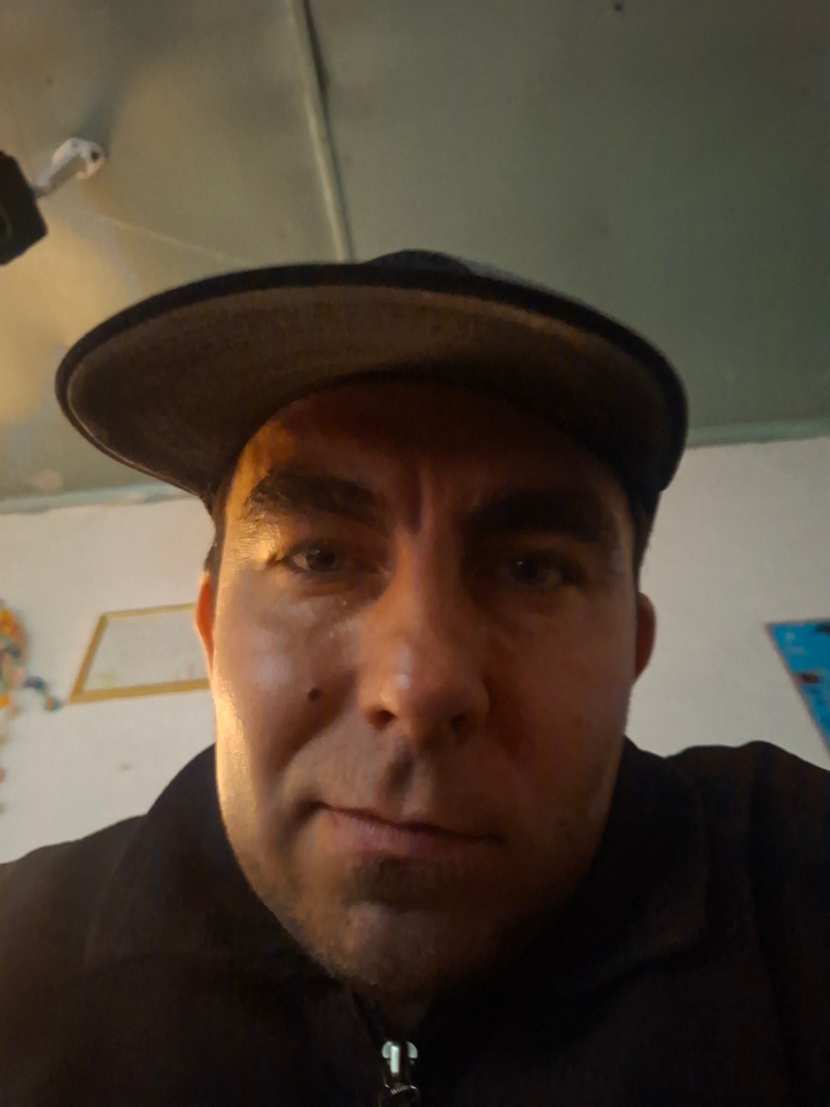 Man in black jacket, baseball cap photographed in selfie