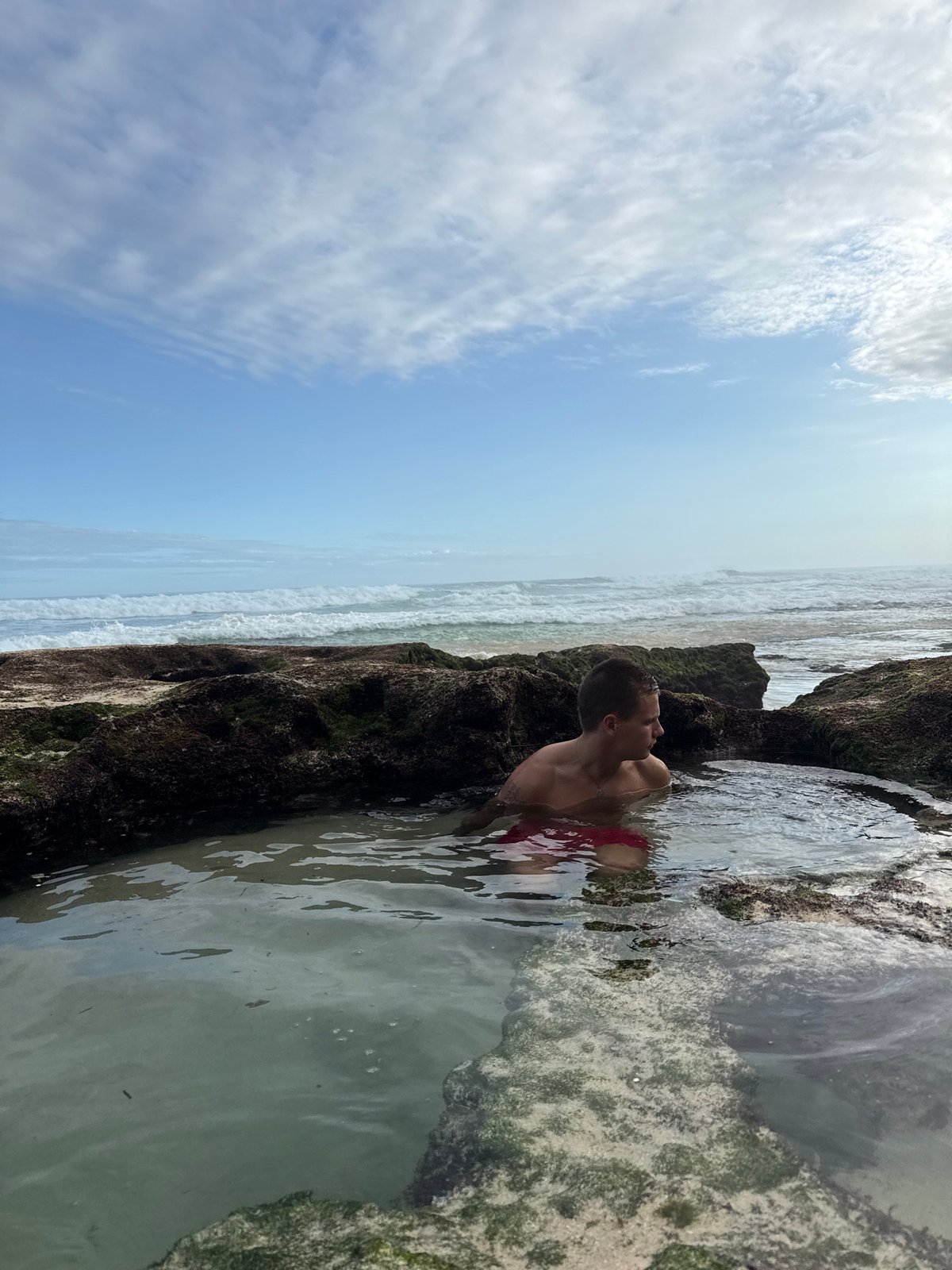 Man explores tide pools at rocky beach in Kuta Selatan