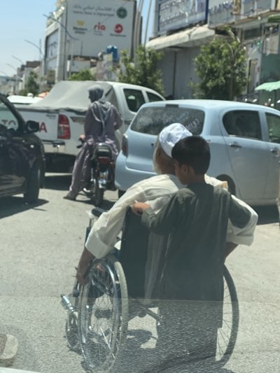 Boy helps elderly man in wheelchair on Kandahar street
