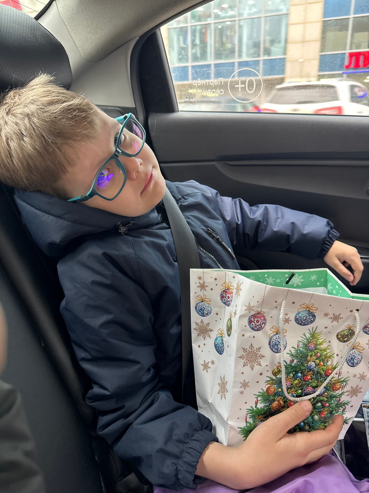 Boy examines Christmas gift bag in car backseat in Perm