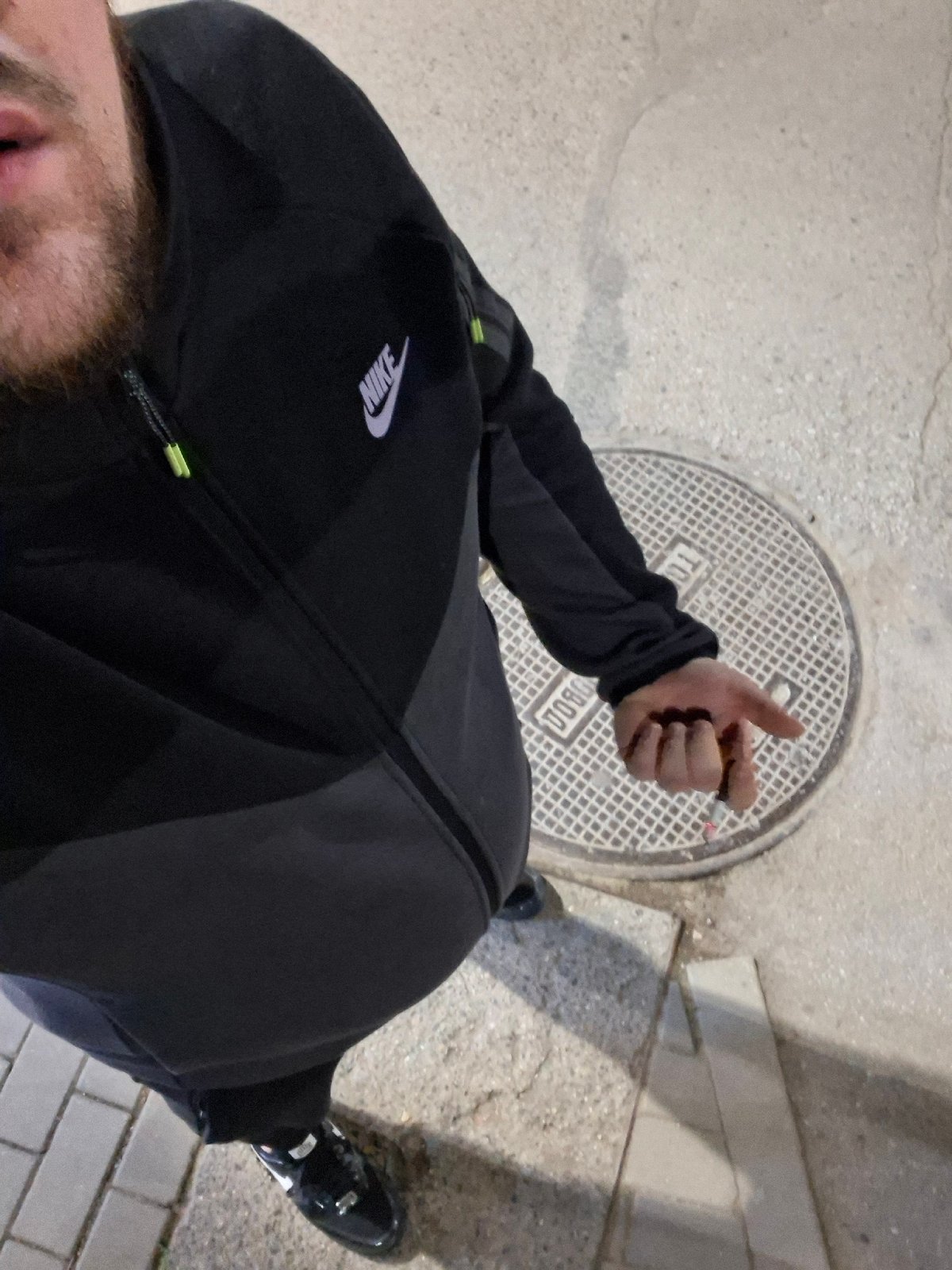 Man in Nike jacket smokes cigarette near manhole in Sofia