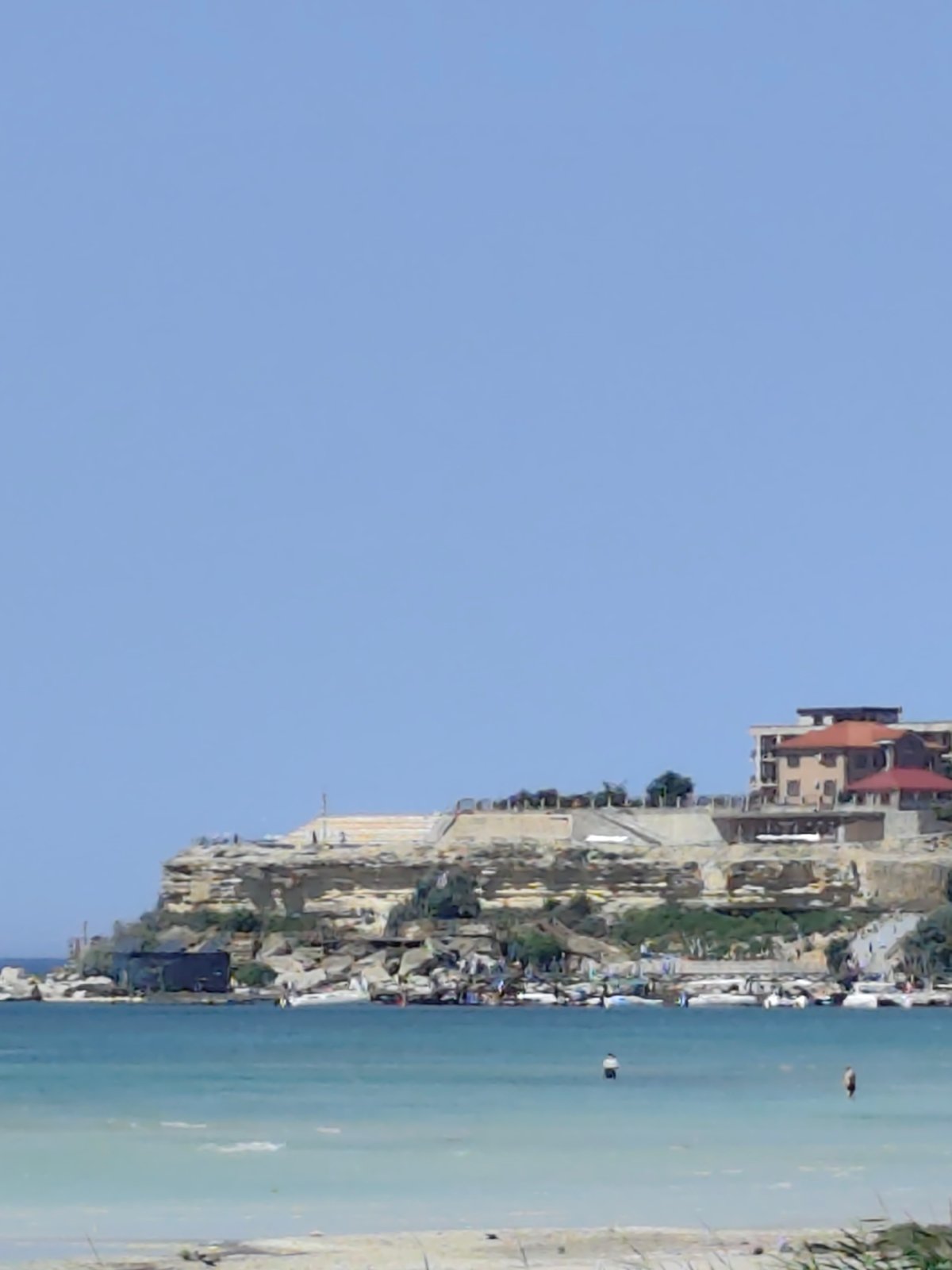 Aktau's Caspian cliffside — buildings, reeds, and calm water
