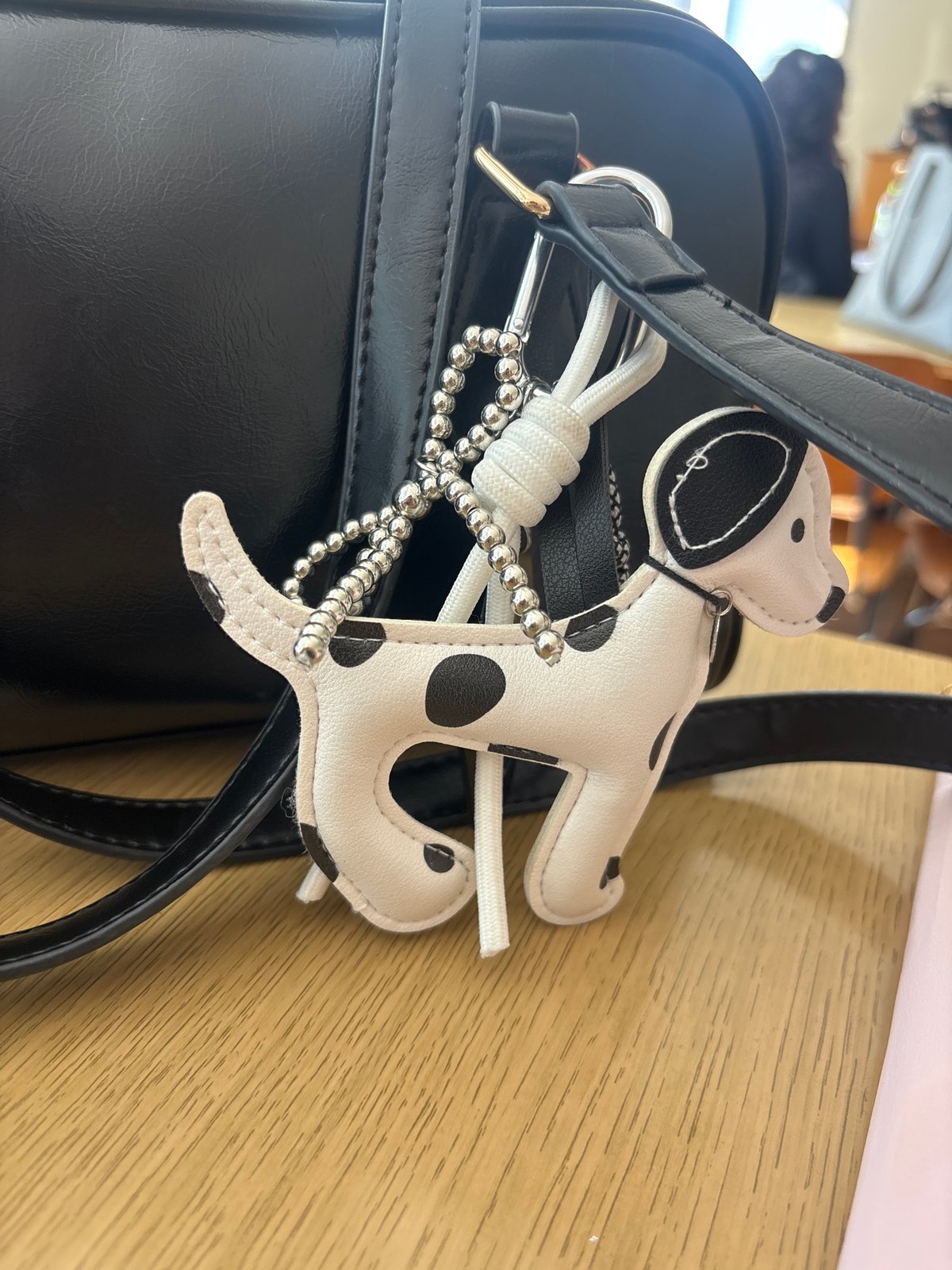 Black handbag spotted with Dalmatian-patterned keyring on wooden surface