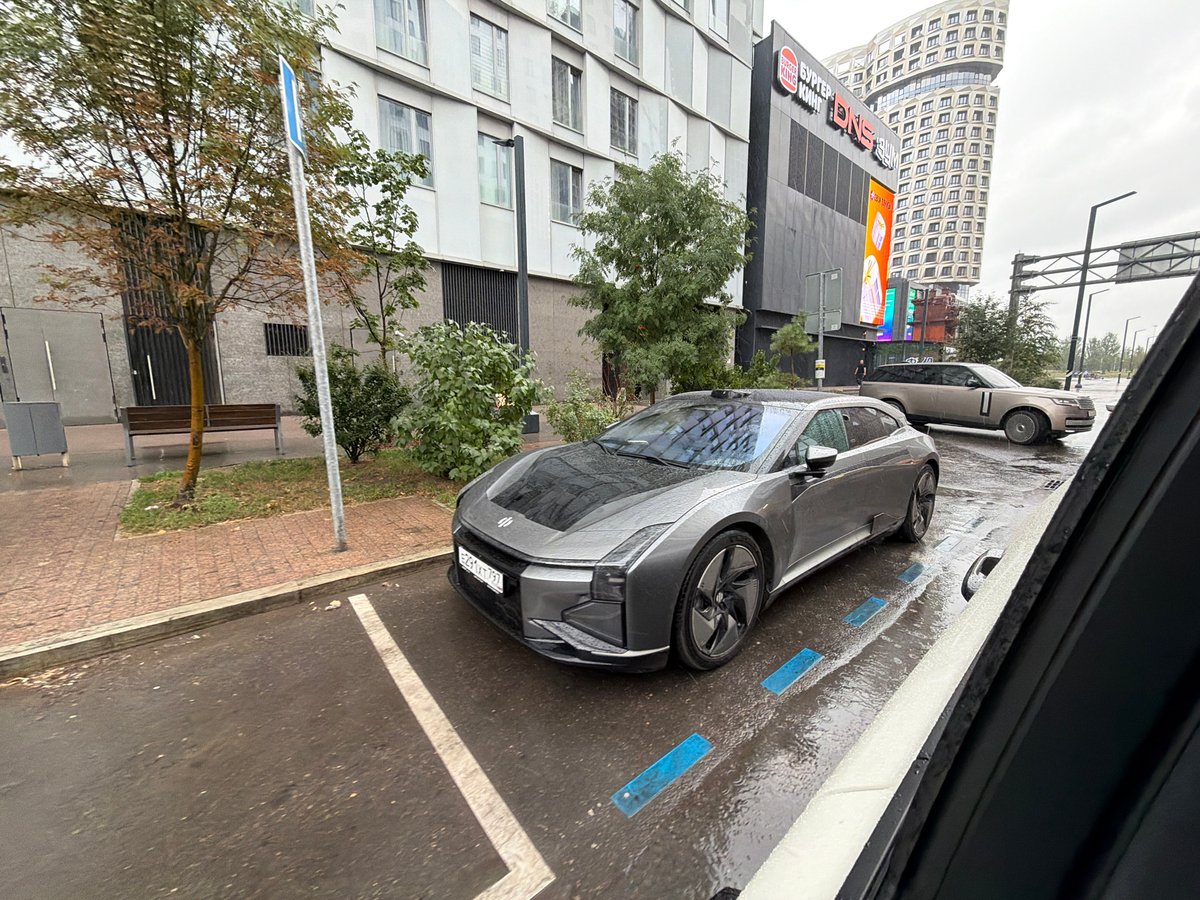 Gray electric car parked on rain-soaked Moscow street with sensors