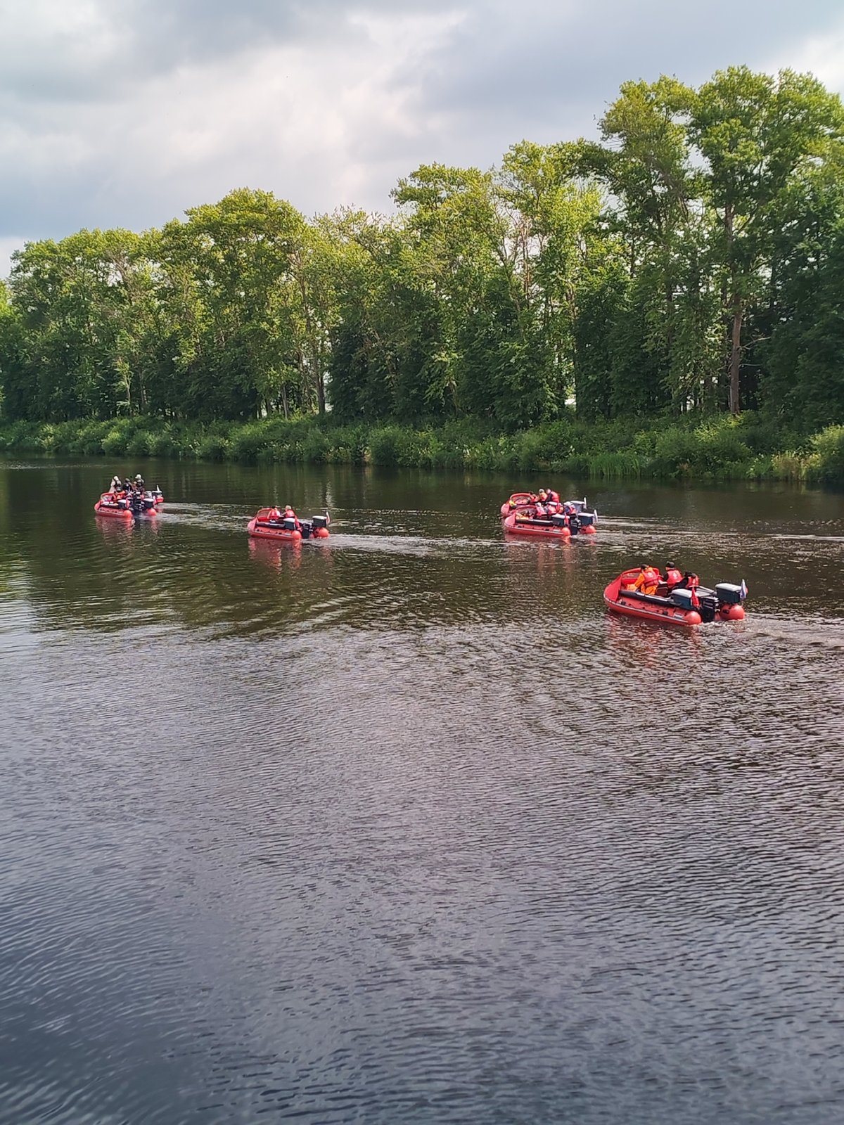 Red inflatable boats travel in convoy down a Russian river