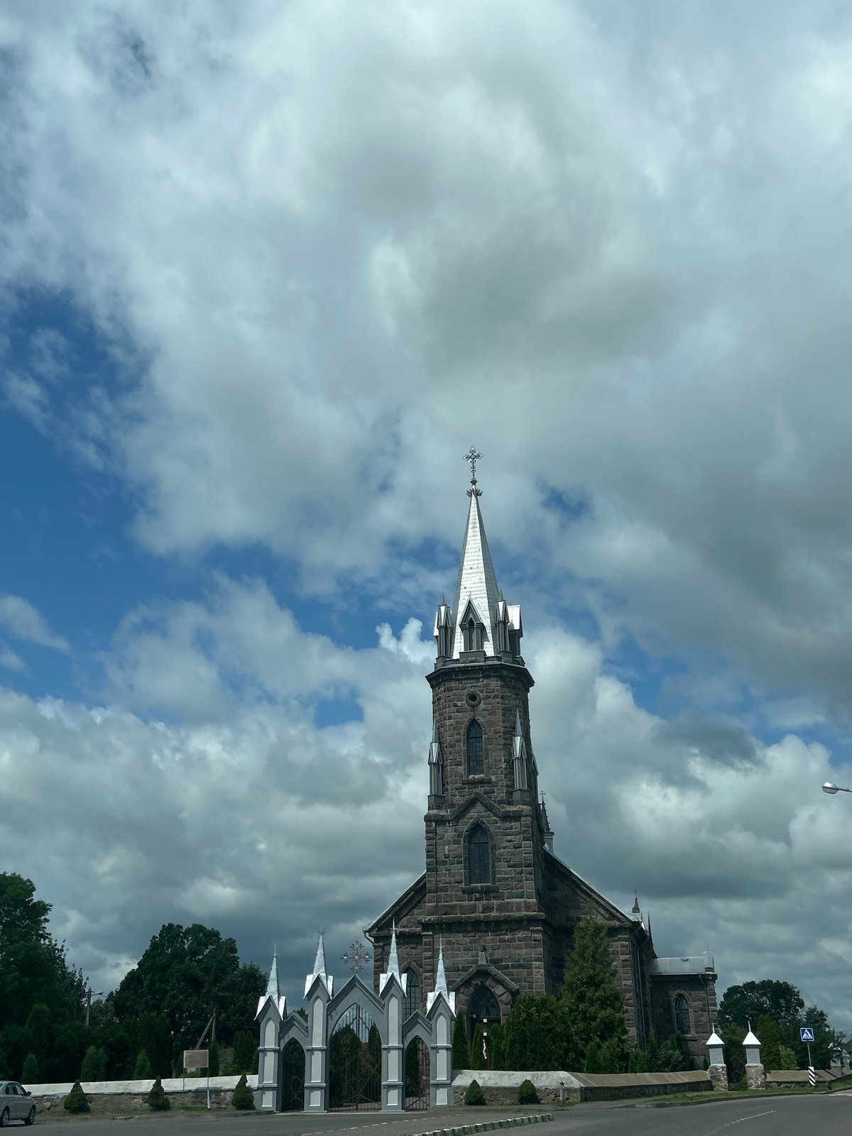 Stone church with pointed spire behind ornate gates, rural Belarus