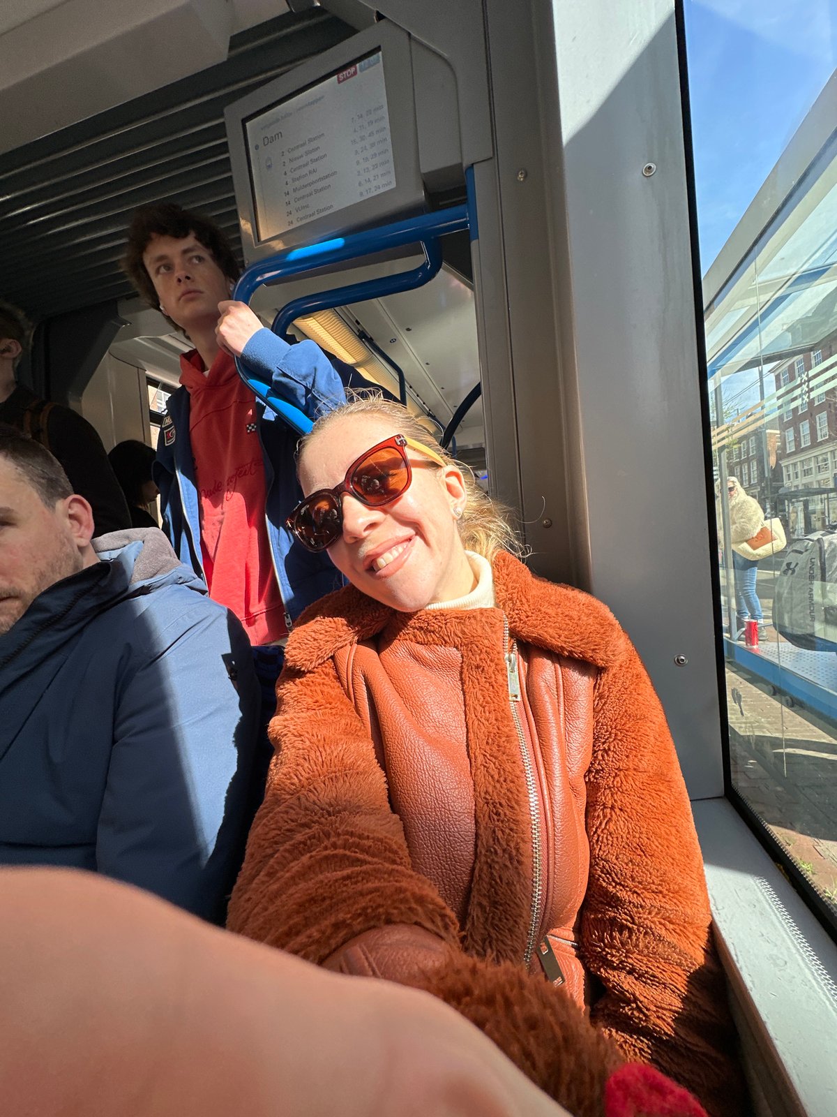 Woman smiles on Amsterdam tram during sunny morning commute