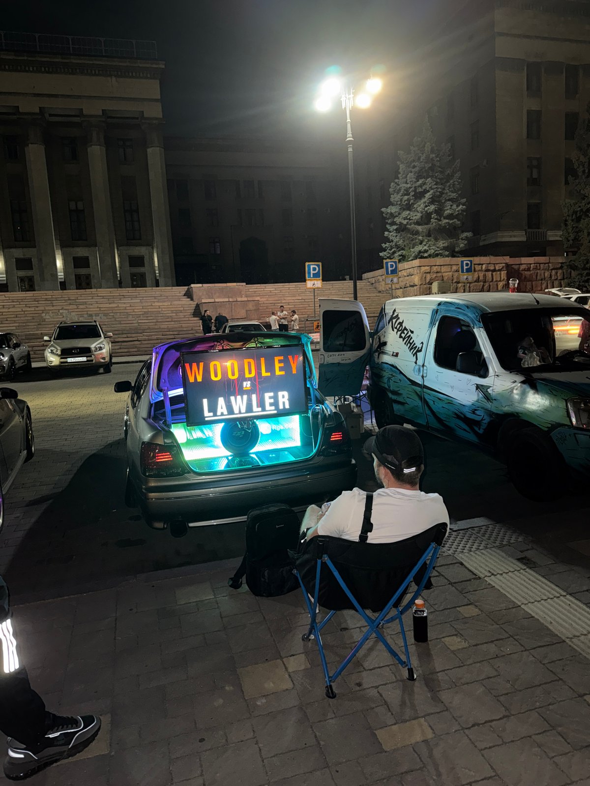 Late-night square hangout with dogs, coffee, and a trunk gaming setup