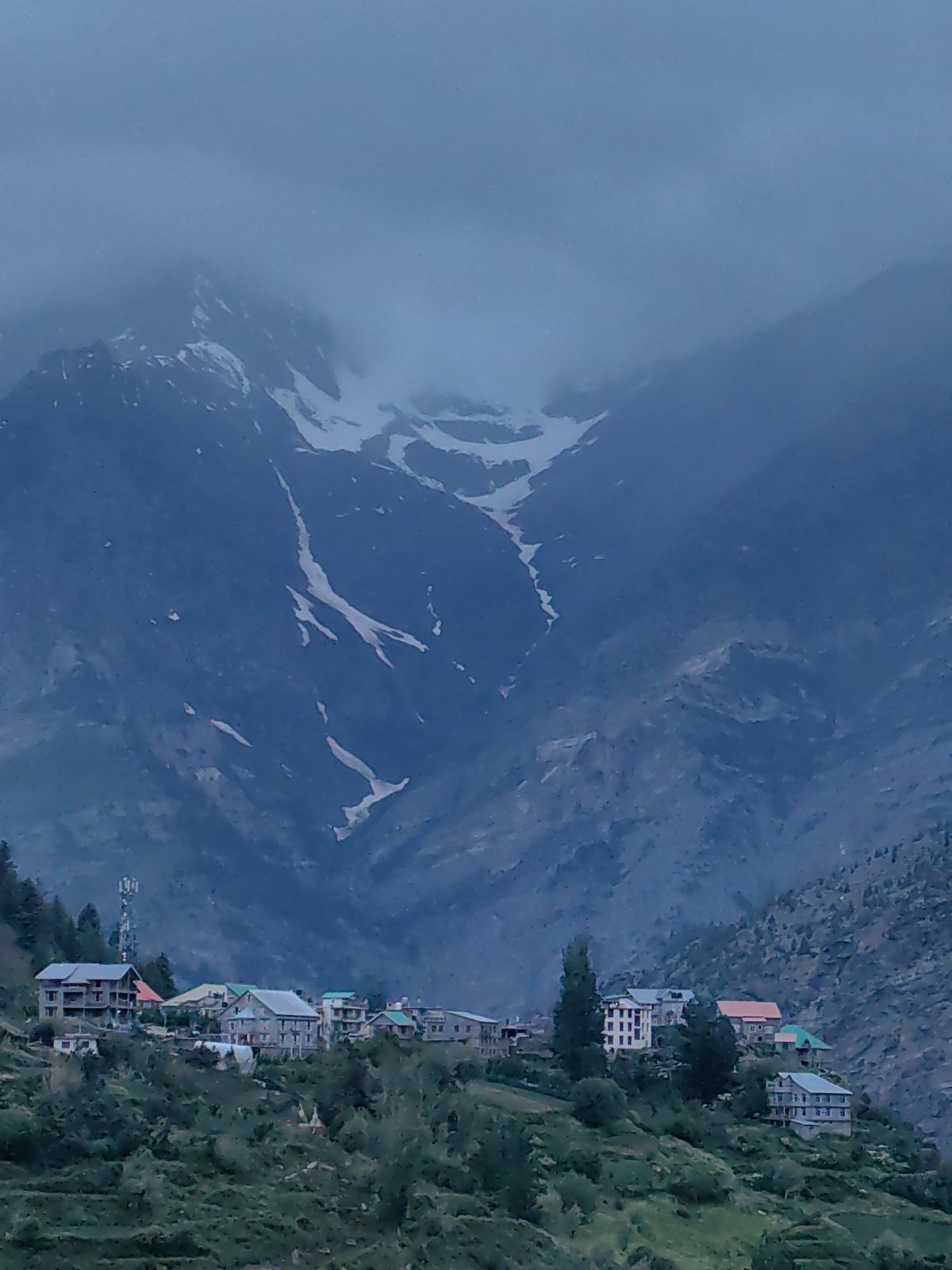 Keylong village under cloudy skies, prayer flags and snowy peaks