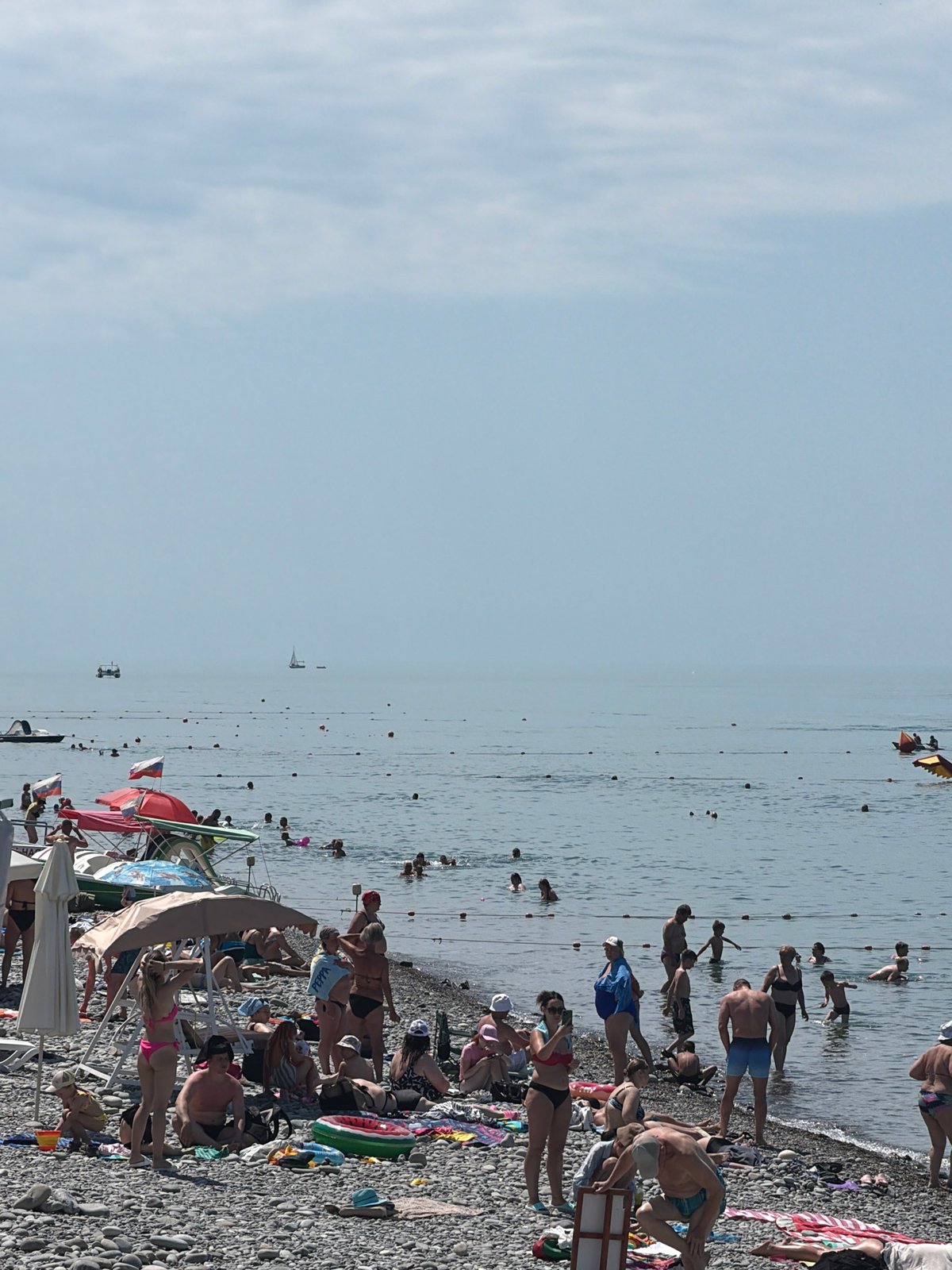 Busy morning at Sochi beach features parasailing, sunbathers