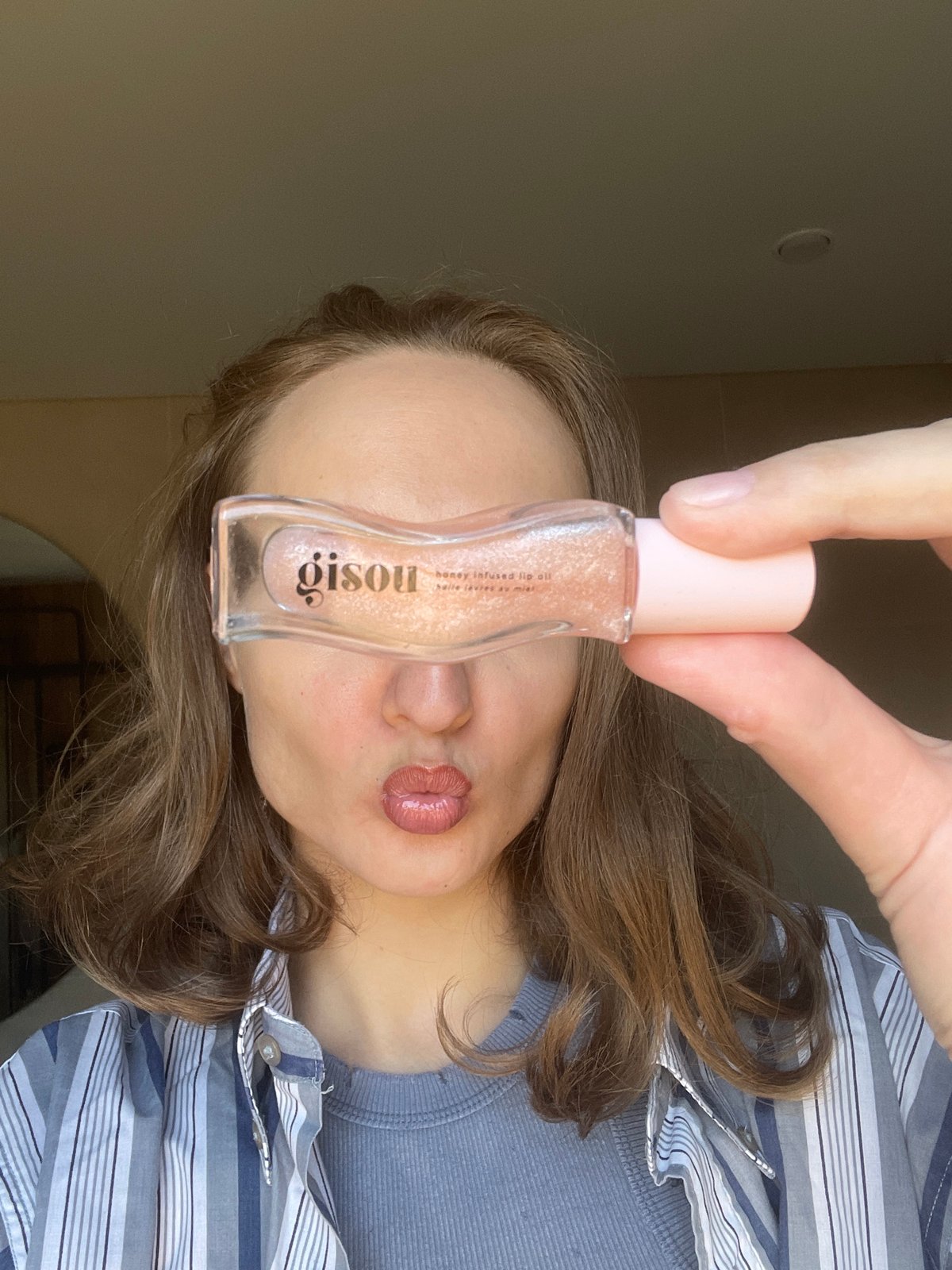 Woman displays Gisou lip oil product in Russian forest area