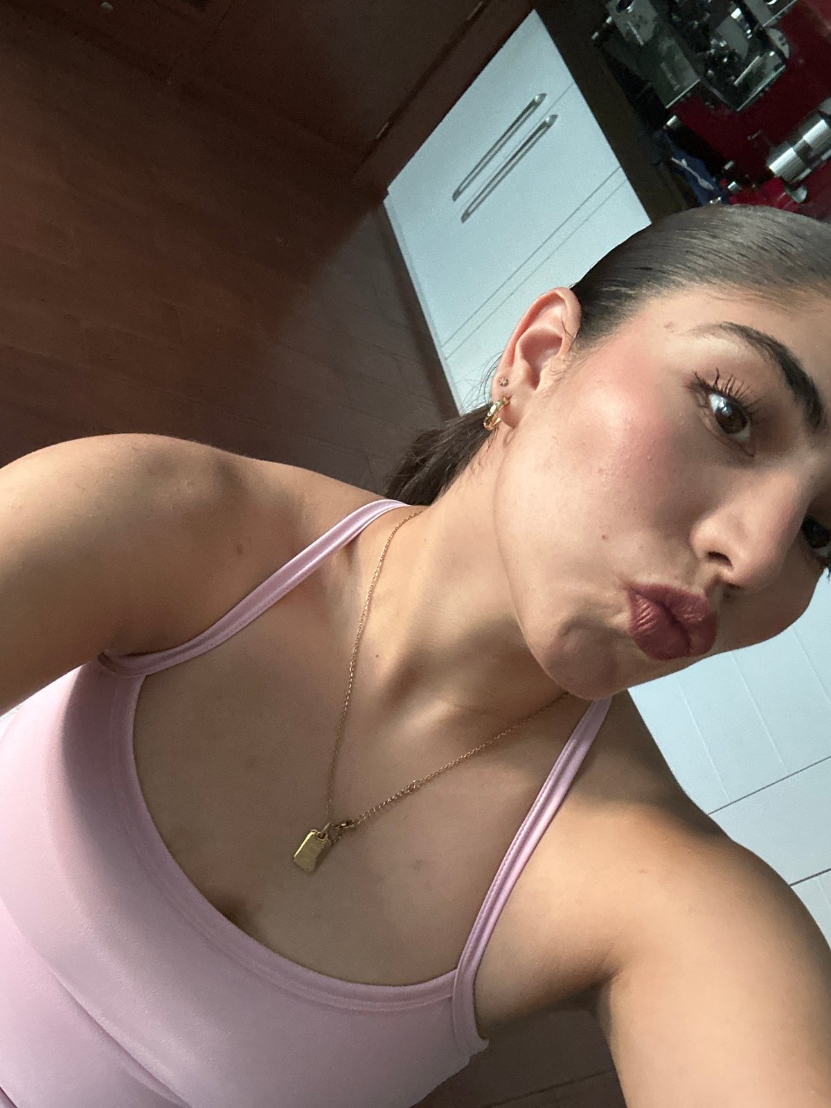 Woman takes selfie indoors wearing pink top and gold jewelry